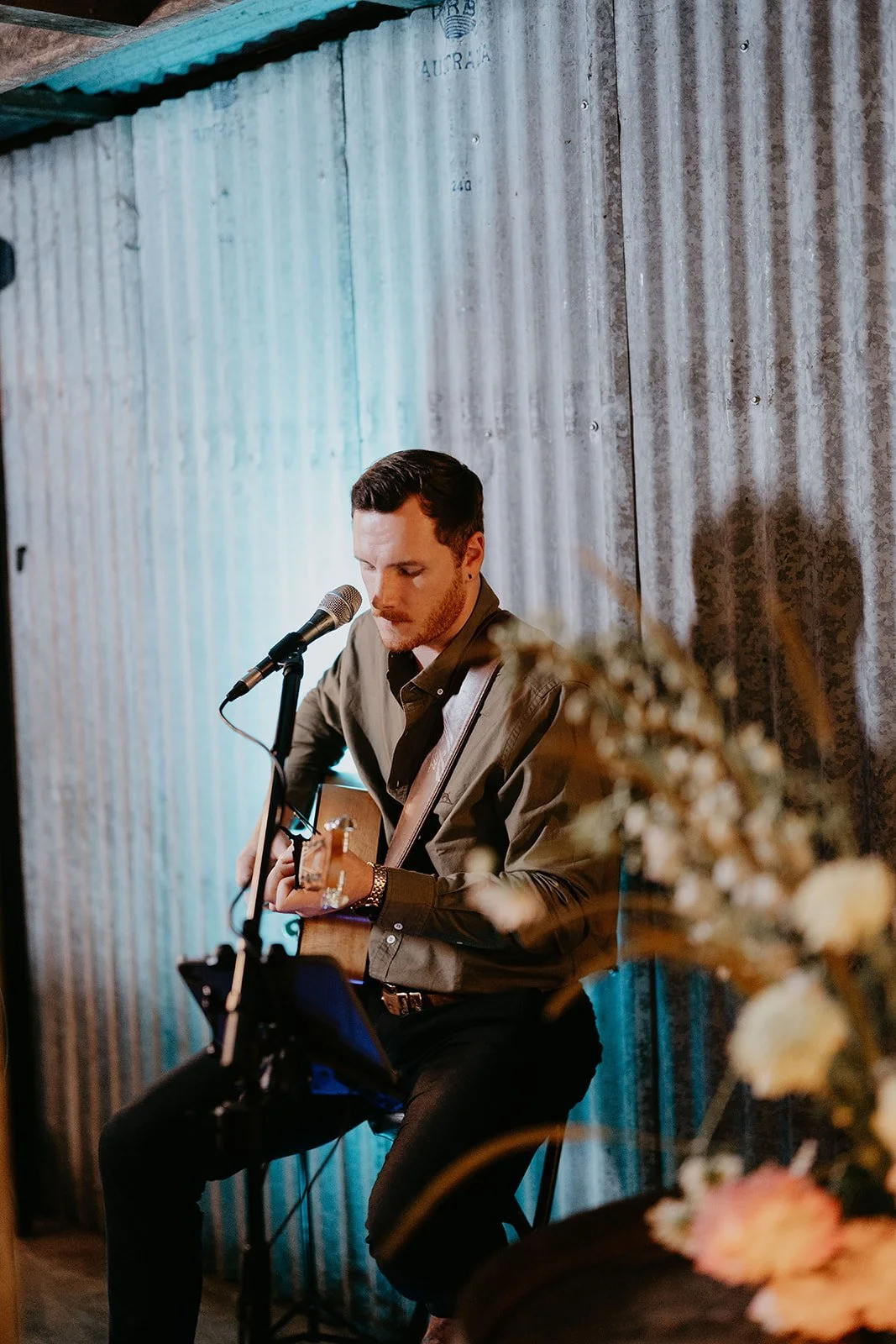 Man playing acoustic guitar and singing into a microphone in a cozy, rustic setting.