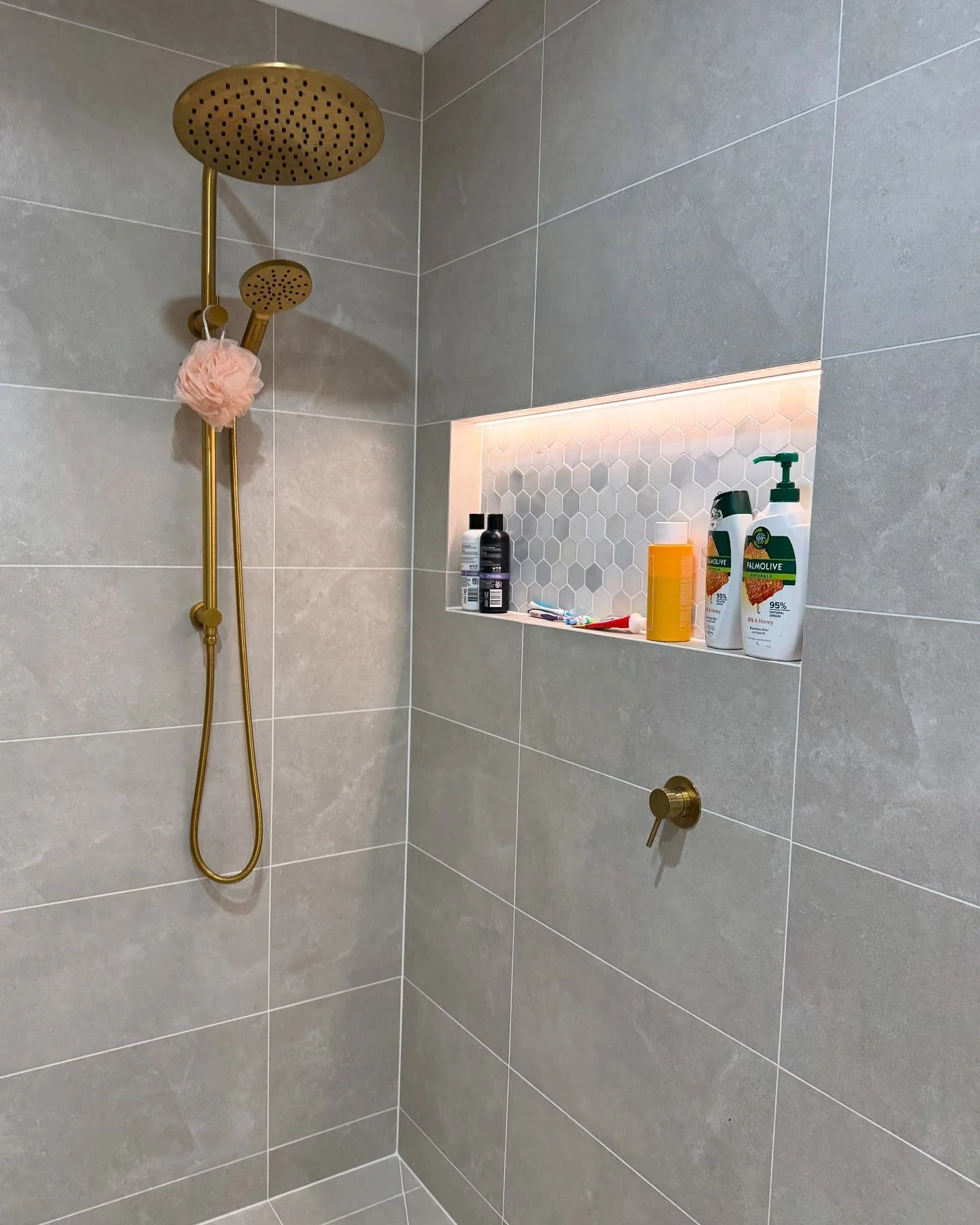Luxury shower installation with premium brushed brass tapware and marble hex mosaic niche tiles.
