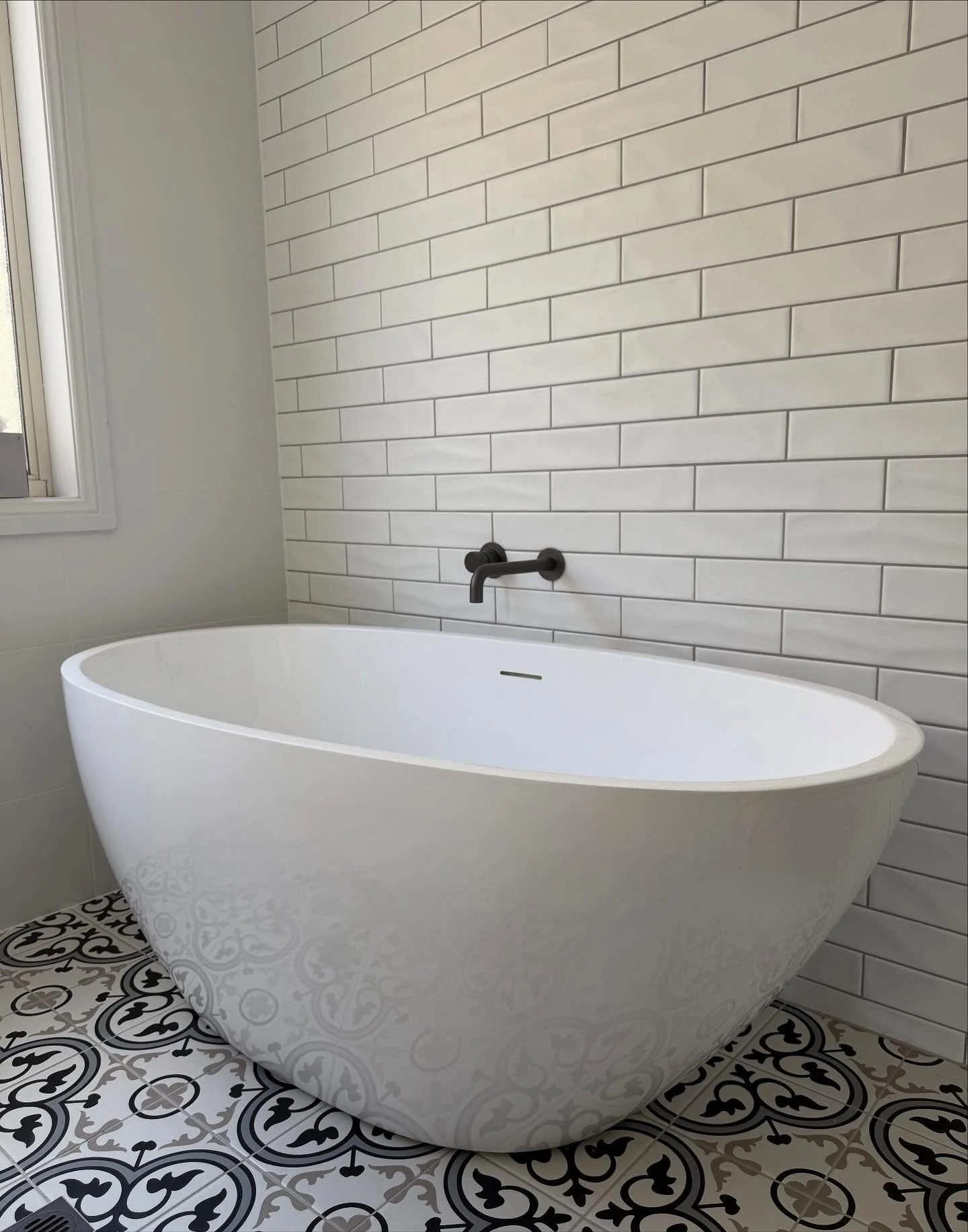Residential bathroom plumbing upgrade featuring a freestanding tub installation and vintage-style patterned floor tiling.
