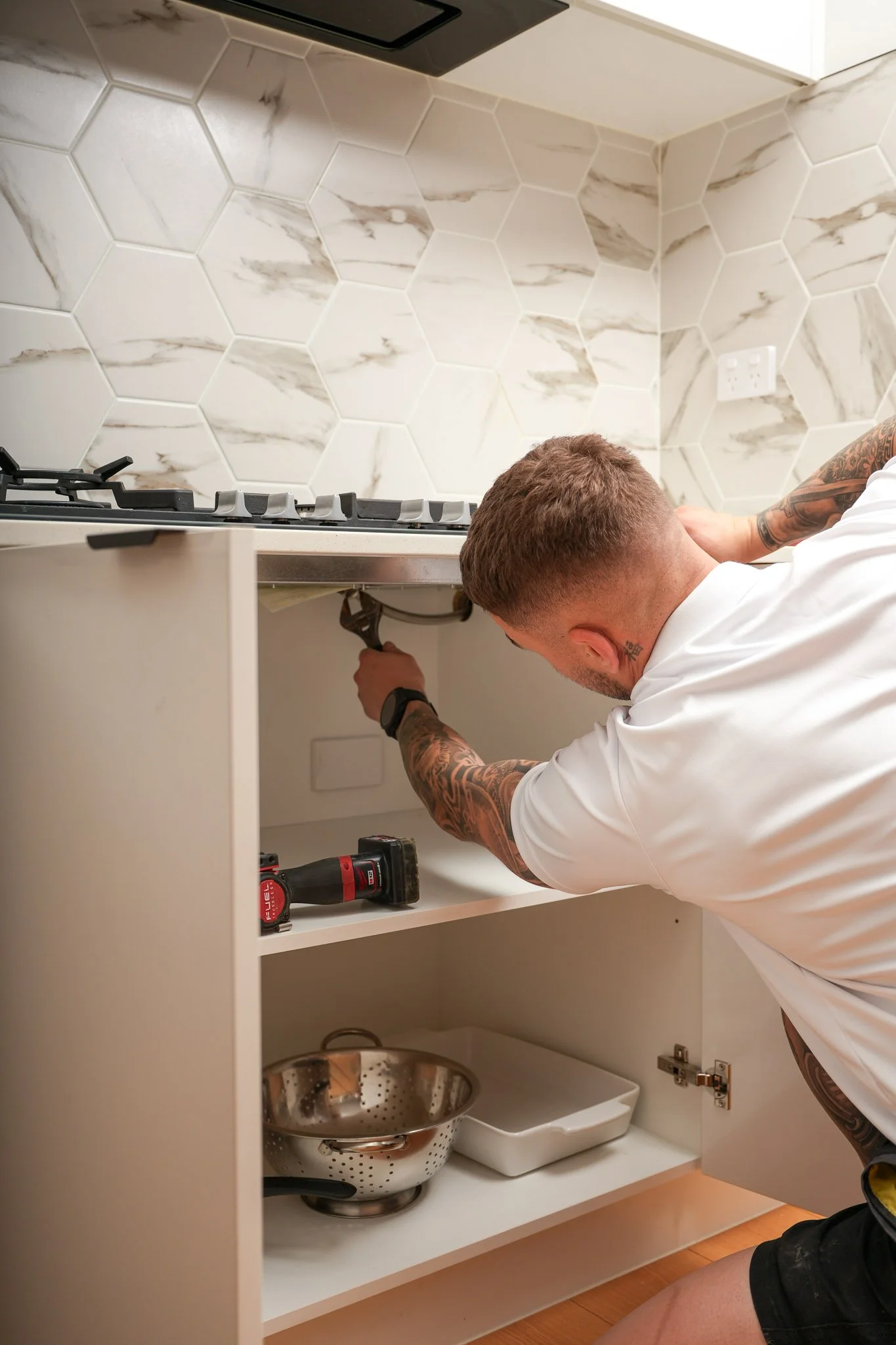 Licensed gas fitter using a spanner to connect gas lines under a kitchen cooktop installation.