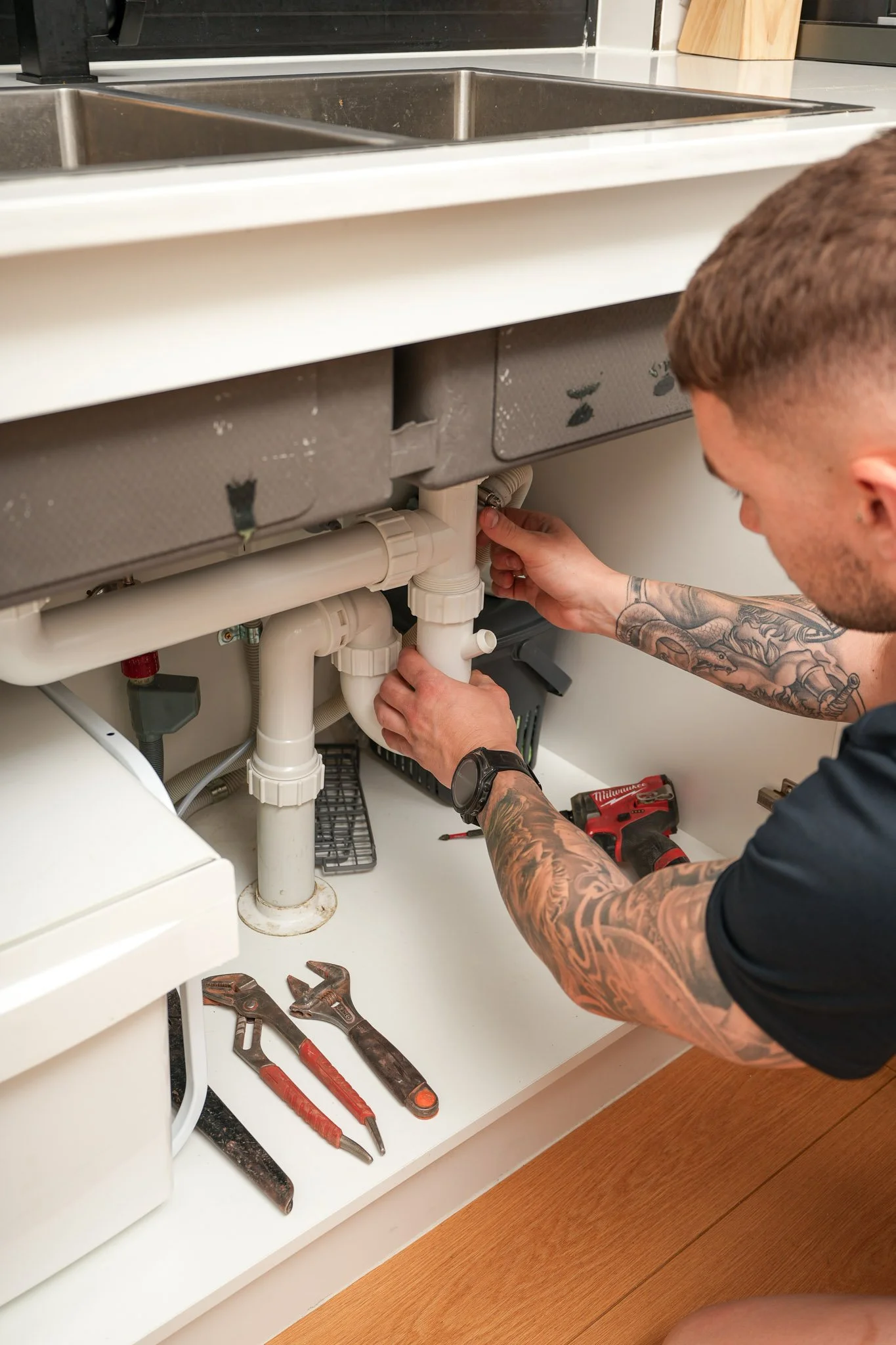 Professional plumber performing general plumbing maintenance under a kitchen sink, fixing pipes and checking for leaks.