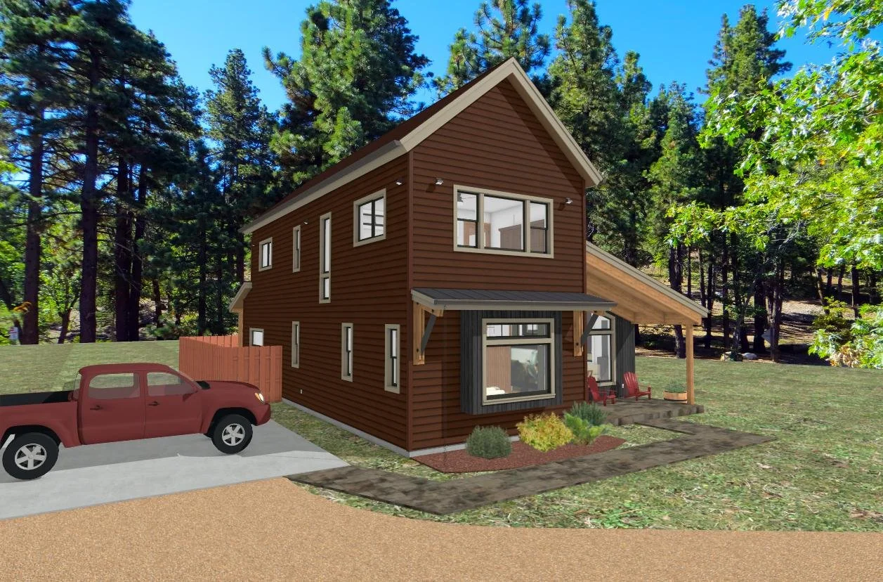 A two-story wooden house with a brown exterior and large windows, situated in a wooded area with tall pine trees, has a small front porch with red chairs and a sloped roof, and a red pickup truck parked in the driveway.