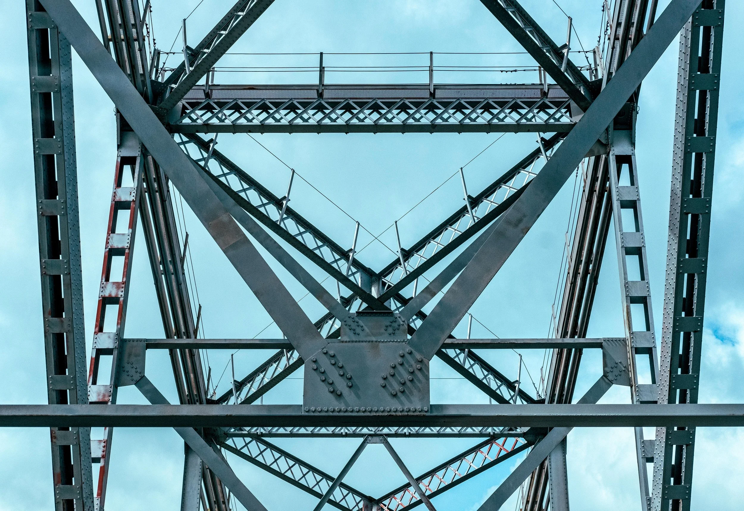 Looking up at the steel framework of a bridge or tower against a cloudy sky.