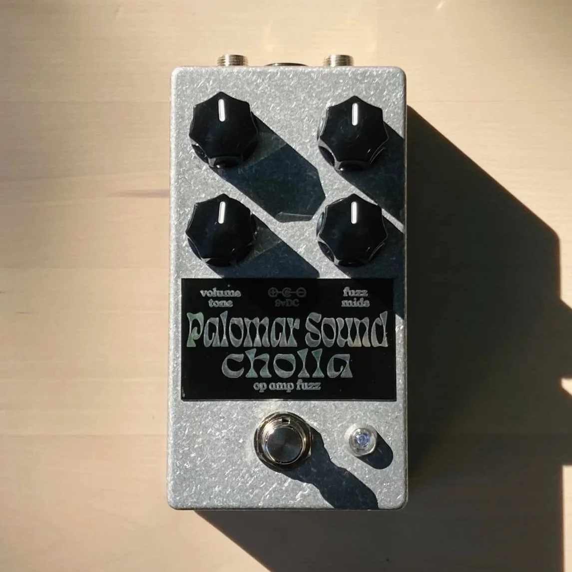 Guitar effects pedal labeled Palomar Sound Cholla with four knobs, a footswitch, and an LED light on a wooden surface.