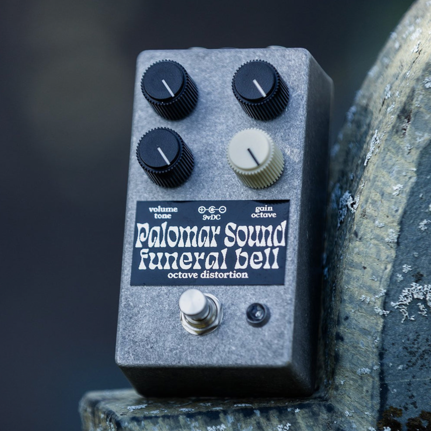 A guitar effects pedal with black and white knobs, labeled Palomar Sound Funeral Bell octave distortion on a rough surface.