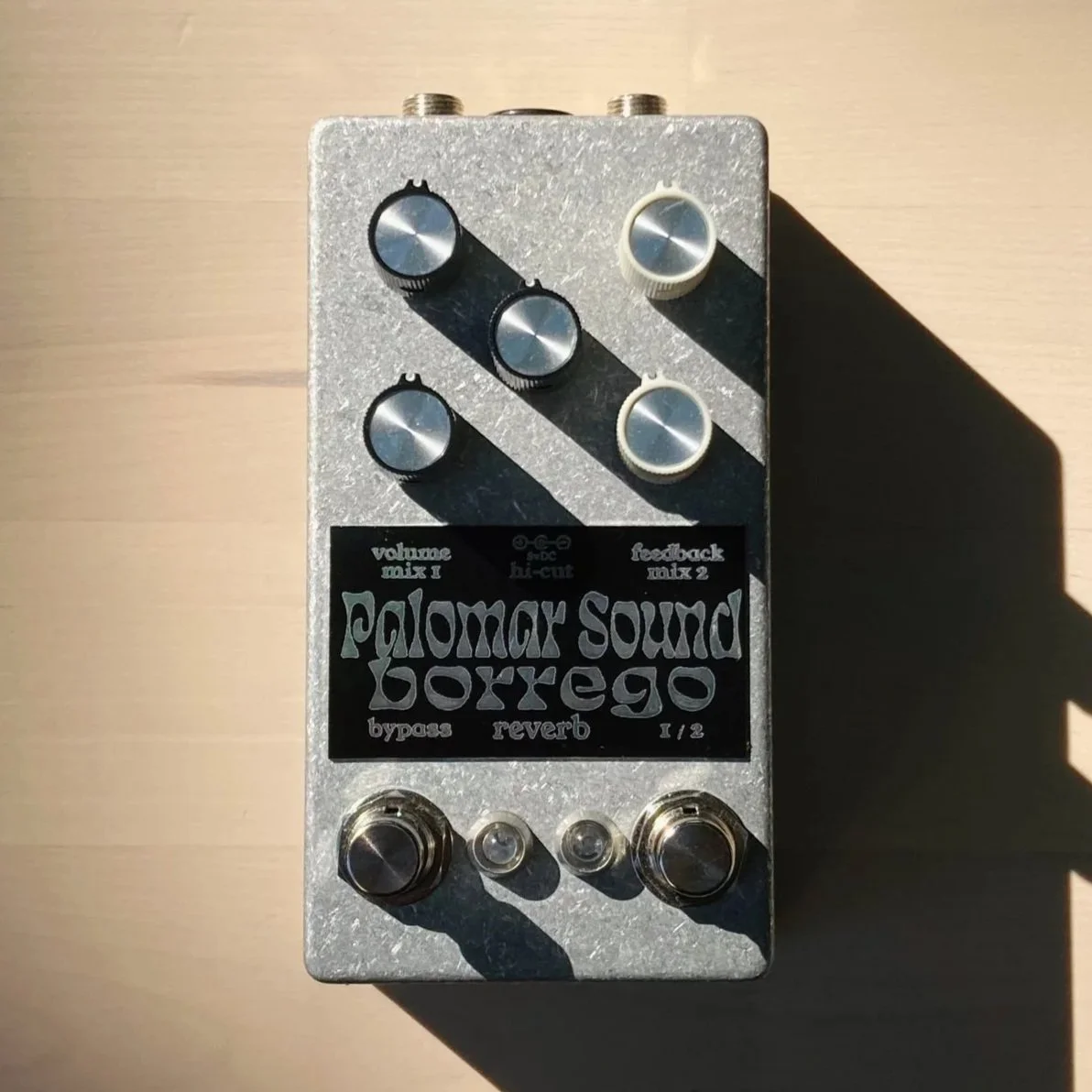 A guitar effects pedal labeled Palomar Sound Borrego with multiple knobs and switches for adjusting sound, placed on a wooden surface.
