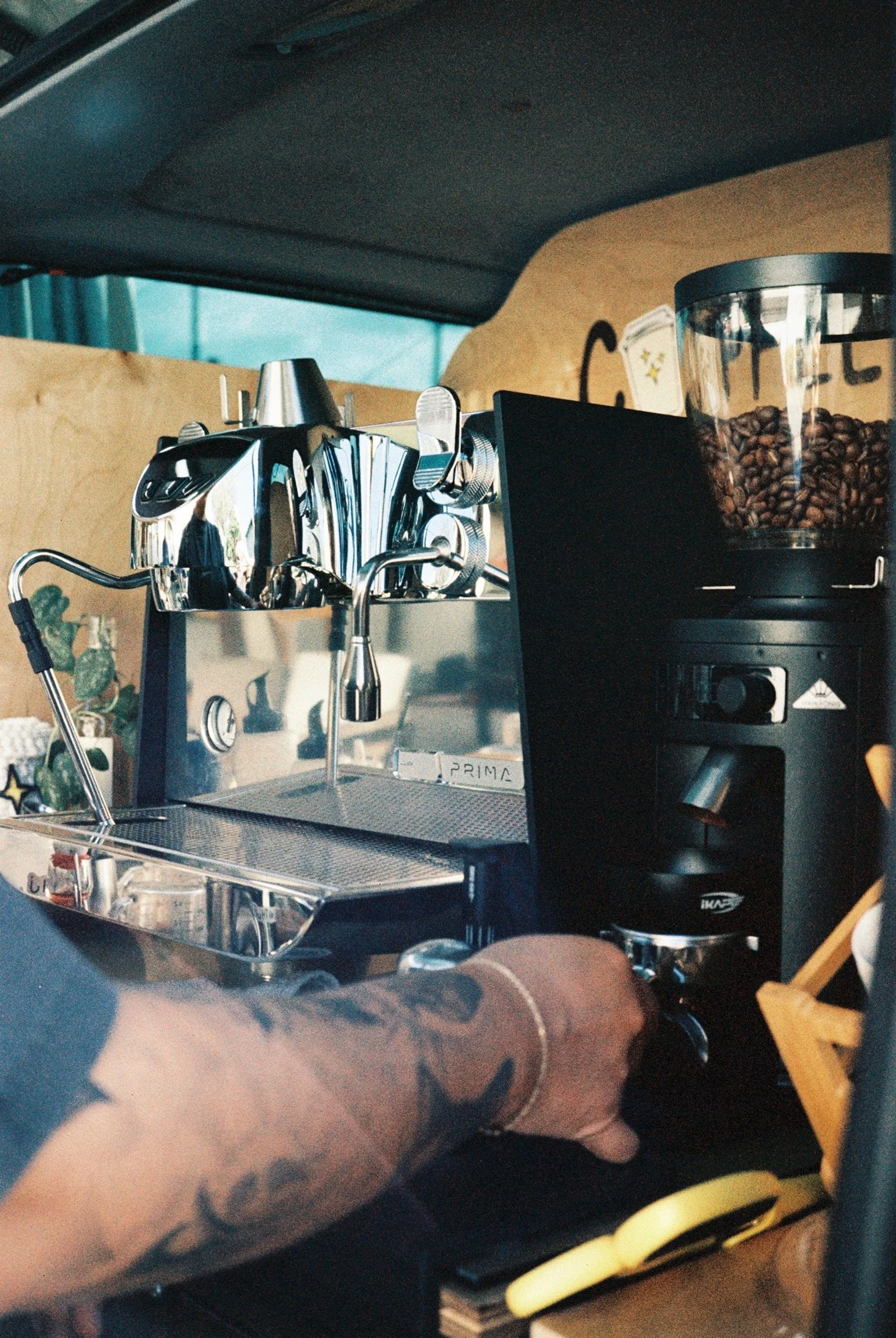 Close-up of a barista operating a professional espresso machine and a coffee bean grinder in a coffee shop or mobile coffee stand.