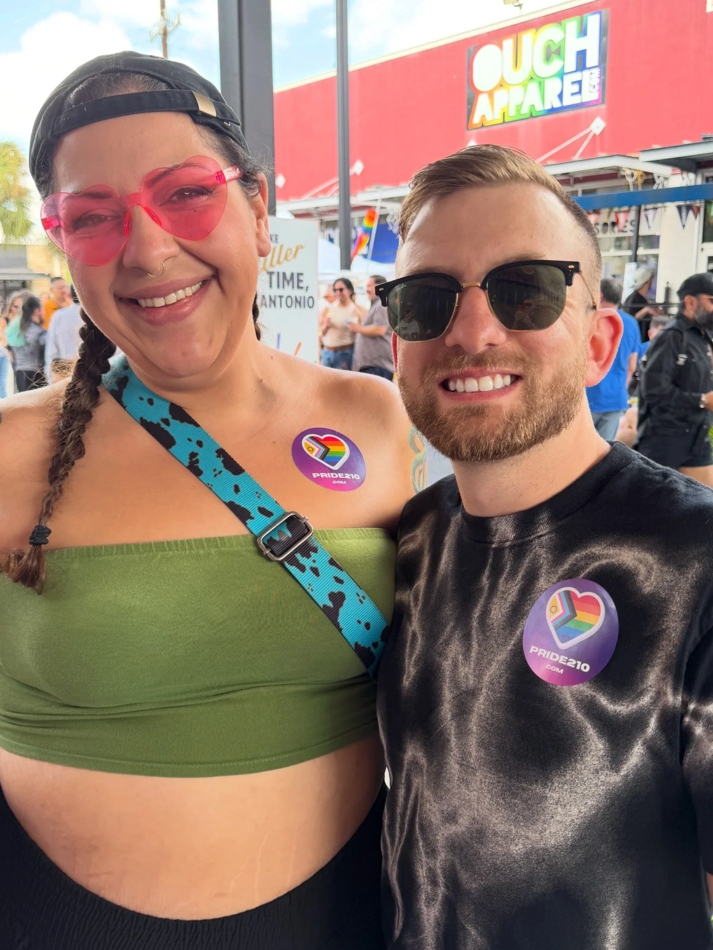 Two attendees at the San Antonio rainbow crosswalk ribbon cutting wearing Pride210.com badges as the LGBTQ+ community gathers to celebrate Pride. This was taken in front of Ouch Apparel.