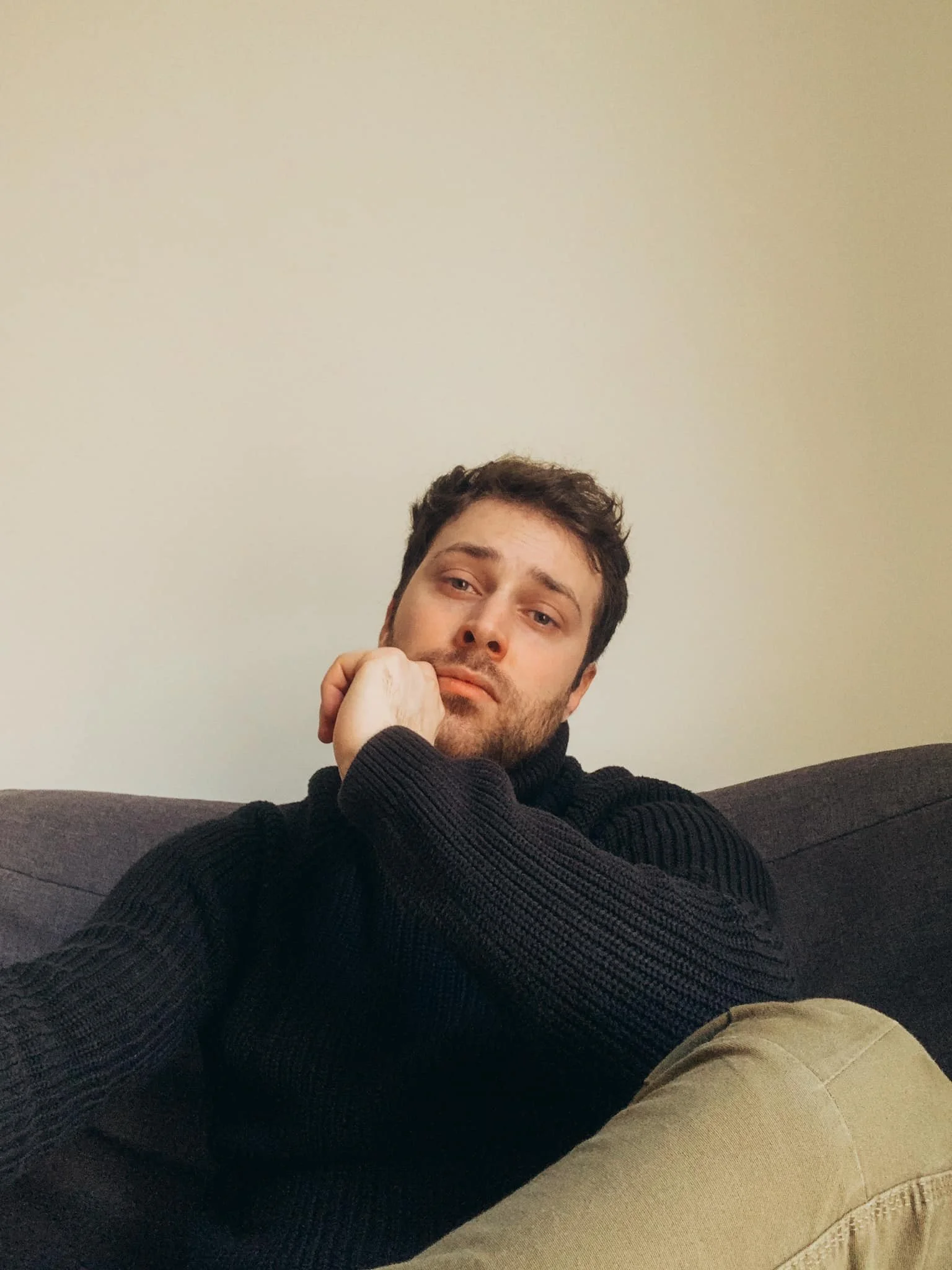 Uomo seduto su un divano, con un abbraccio e una espressione pensierosa, indossa un maglione nero