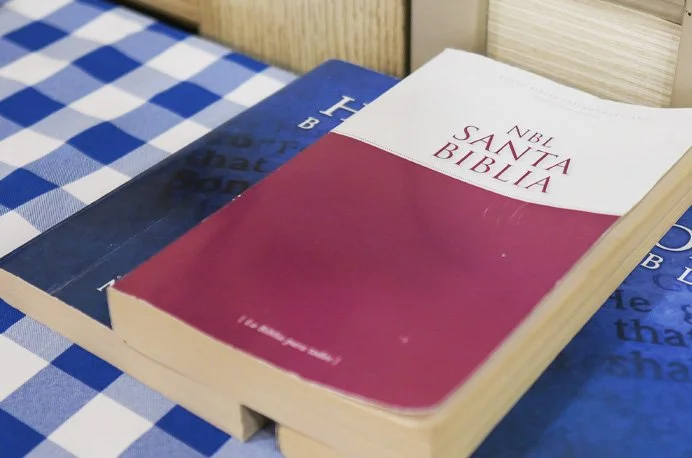 A Bible resting on a blue book, placed on a checkered tablecloth.