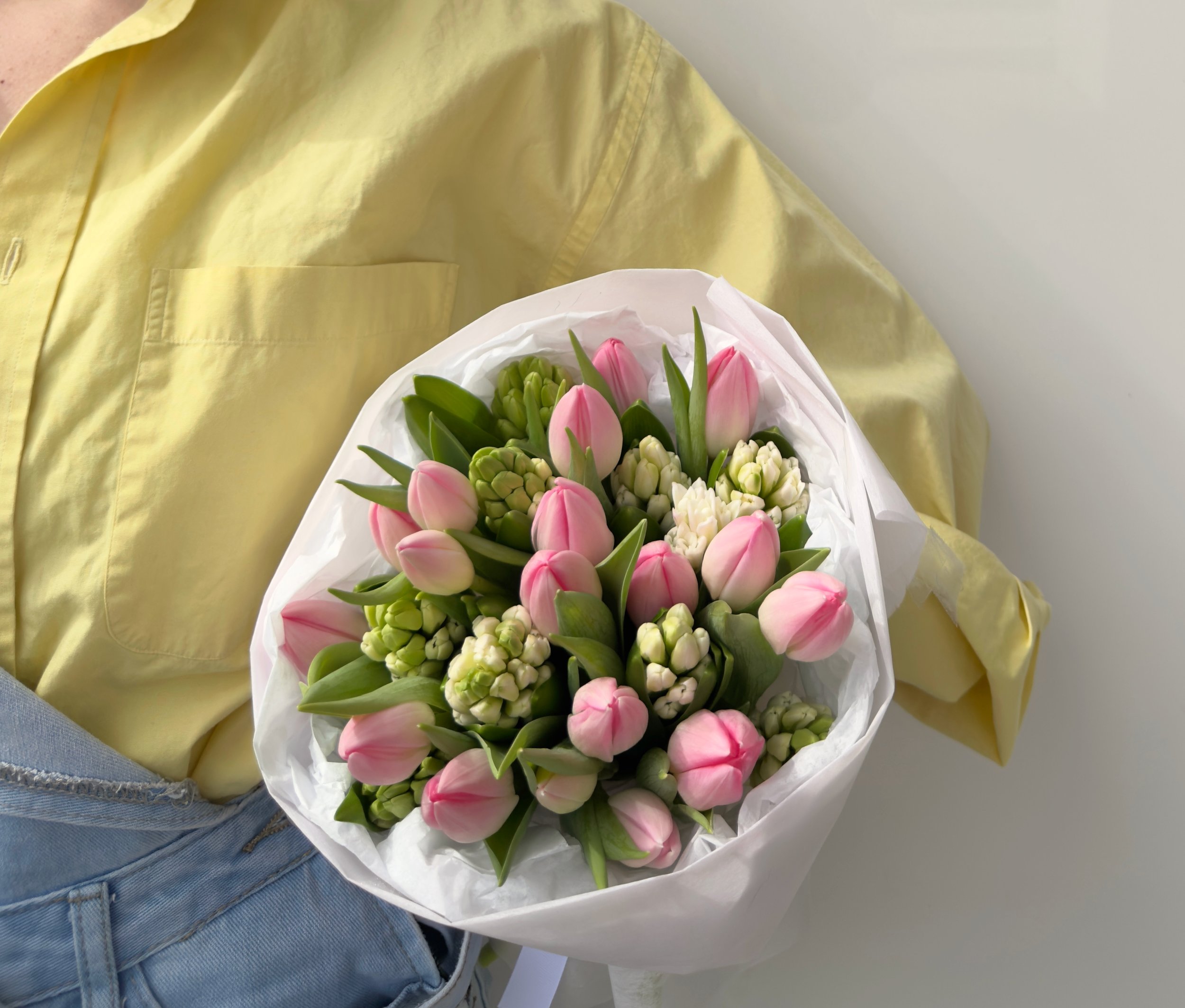 Person in yellow shirt holding a bouquet of pink and white flowers.