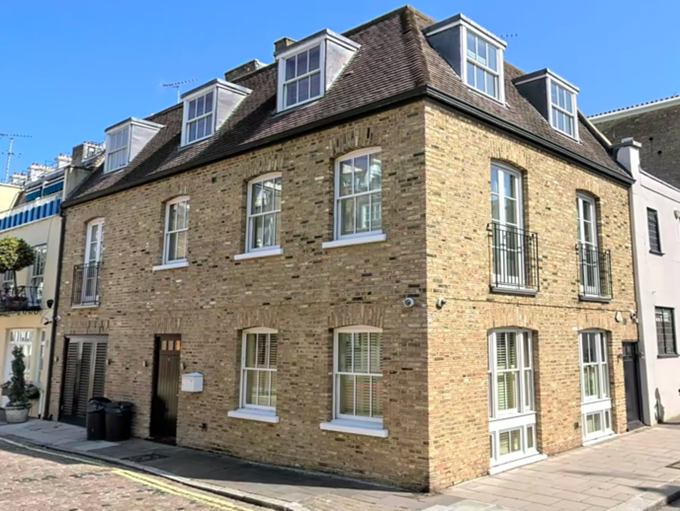 Brick residential building with multiple windows and small balconies on the upper floors, located on a cobblestone street under a clear blue sky.