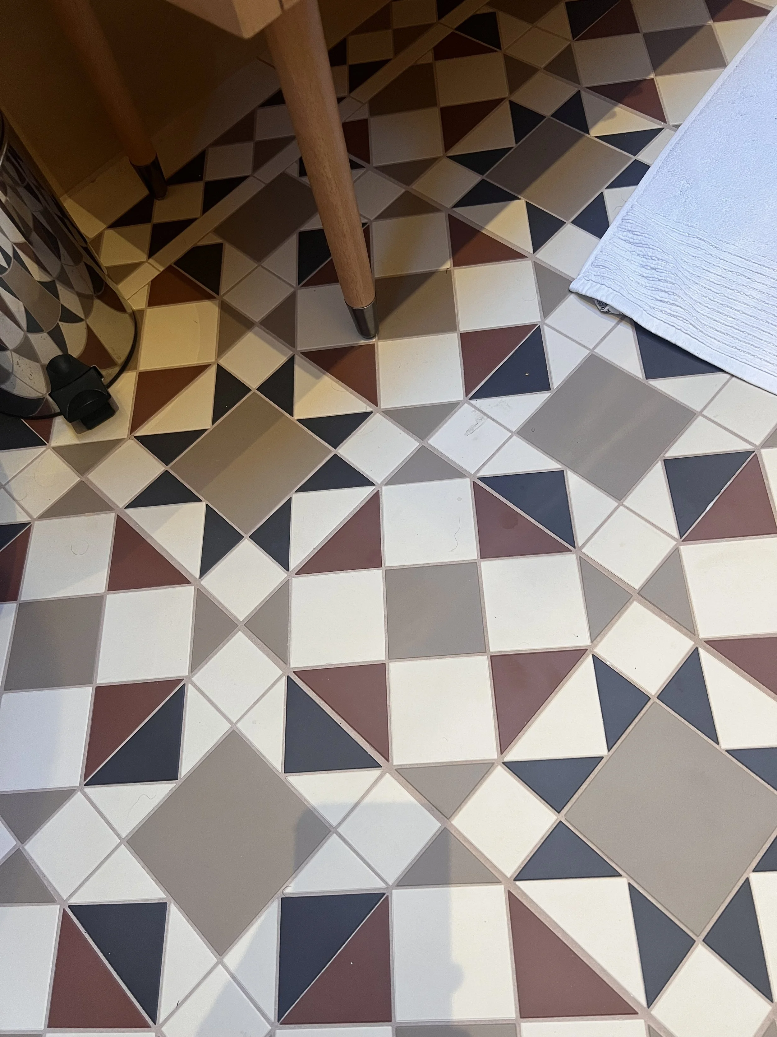 Patterned floor tiles with geometric shapes in colors including white, black, beige, and maroon, and a white textured mat partially visible on the right side.