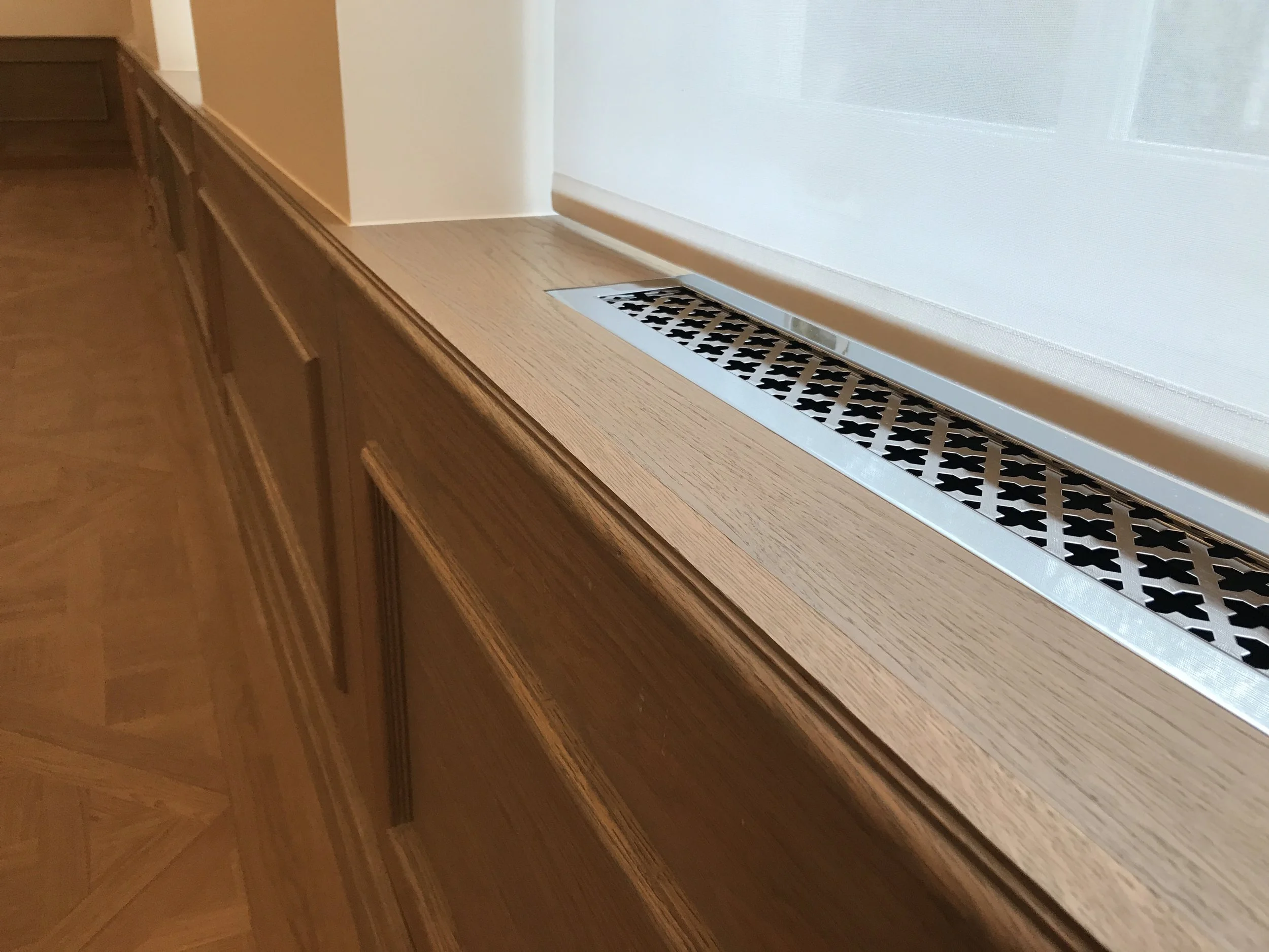 Close-up of a wooden windowsill with a metal air vent grate in the gap between the window and the sill.
