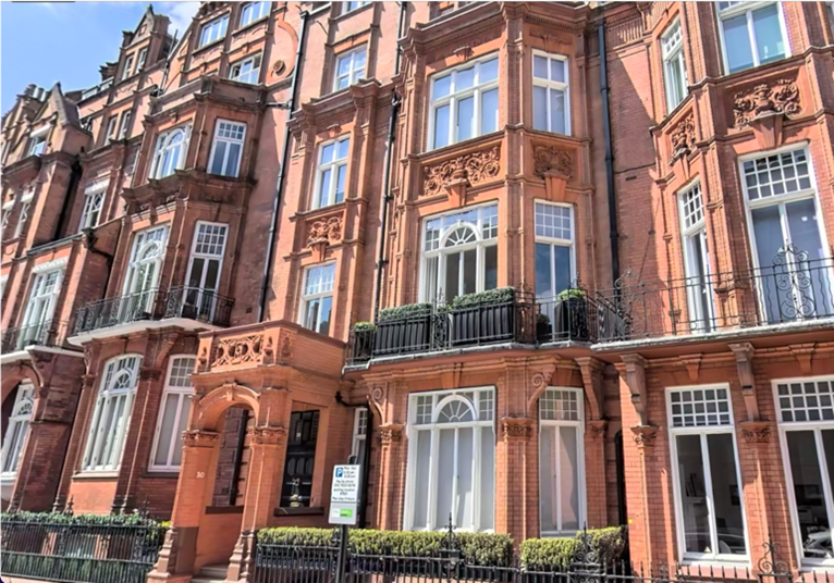 Red brick historic apartment building with multiple floors, large windows, decorative architectural details, balconies, and potted plants