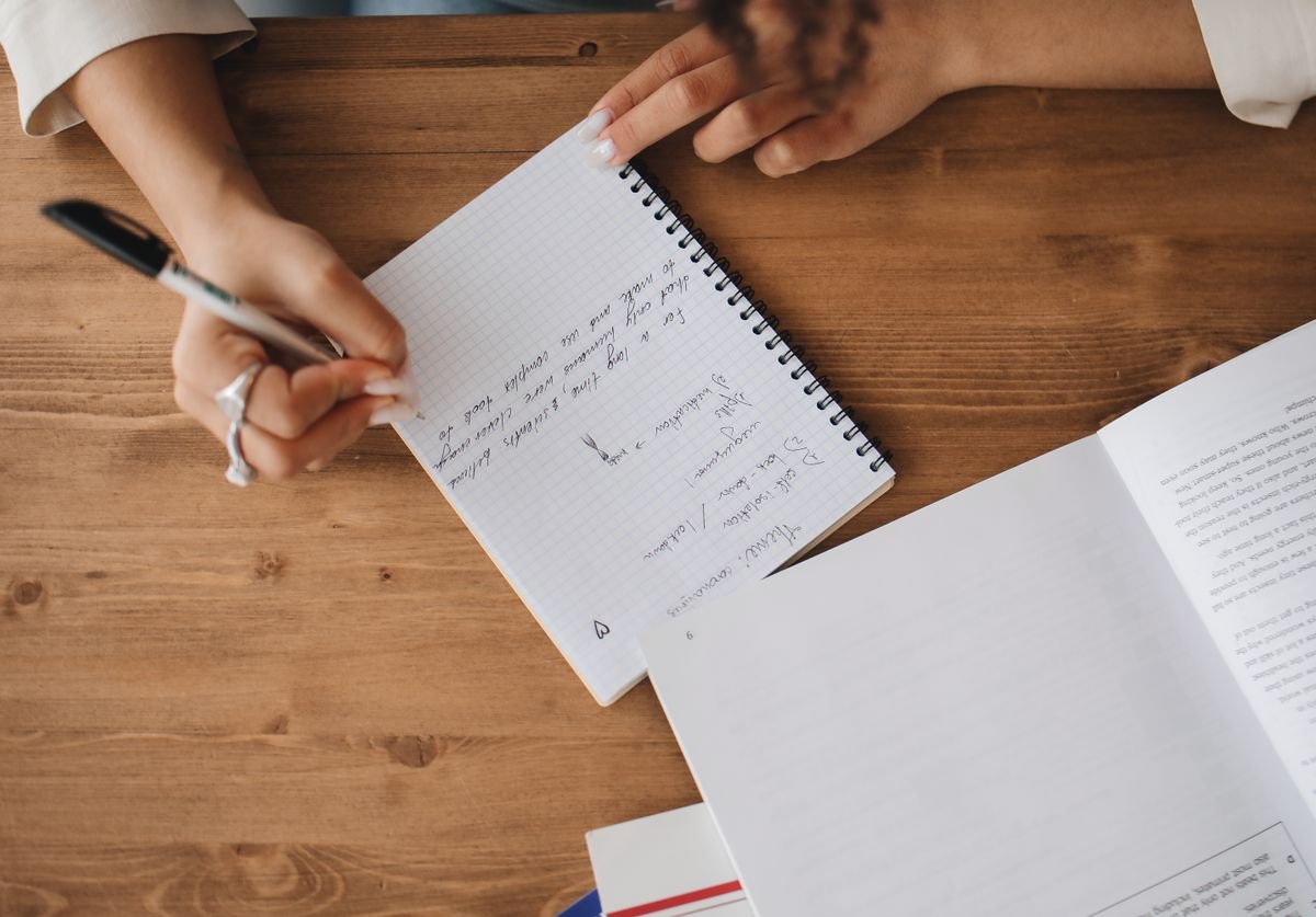 a-woman-writing-notes-on-a-notebook-on-a-wooden-table.jpg