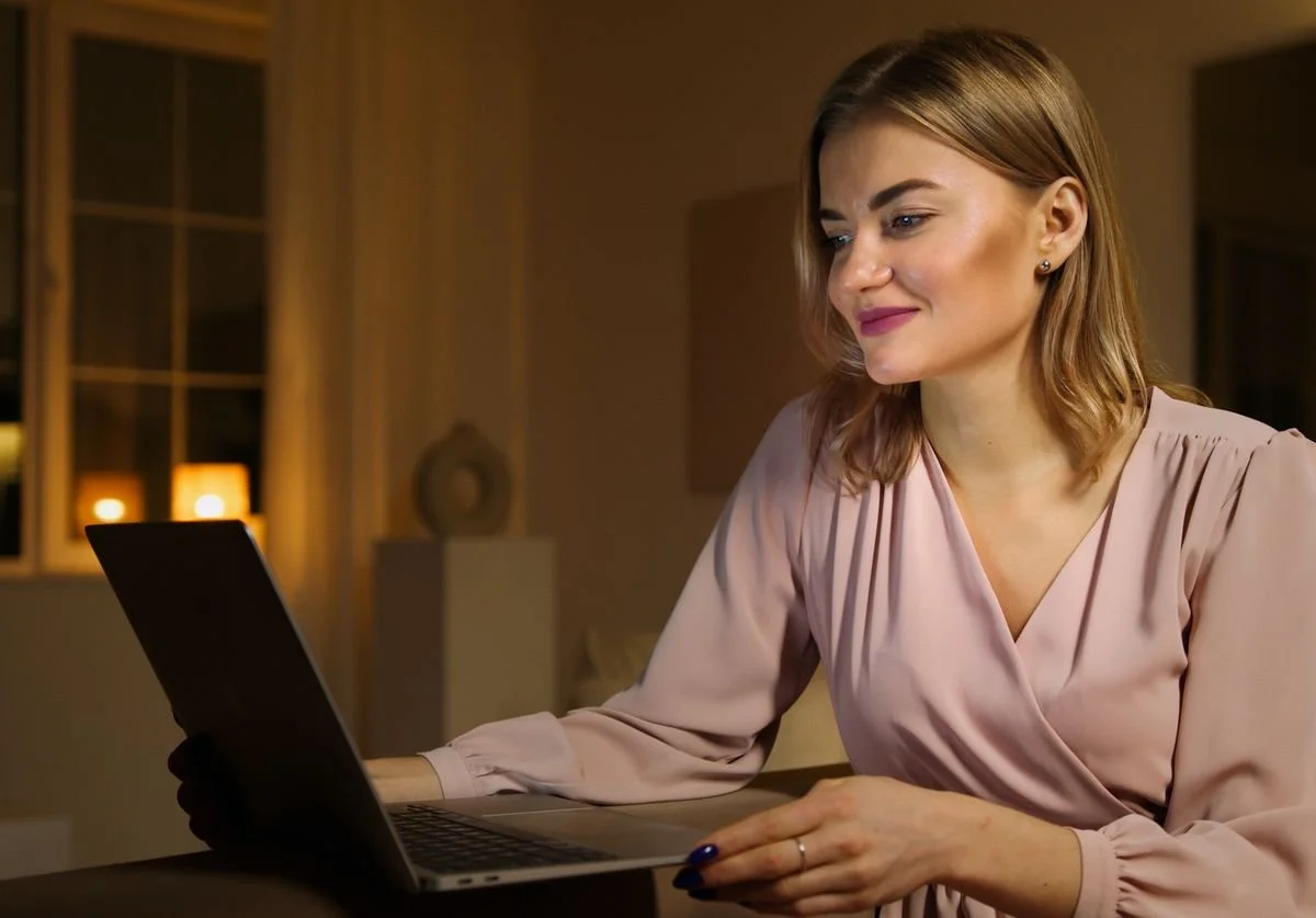 woman-smiling-while-looking-at-laptop-in-dim-lit-room-nomadic-virtual-solutions.jpg