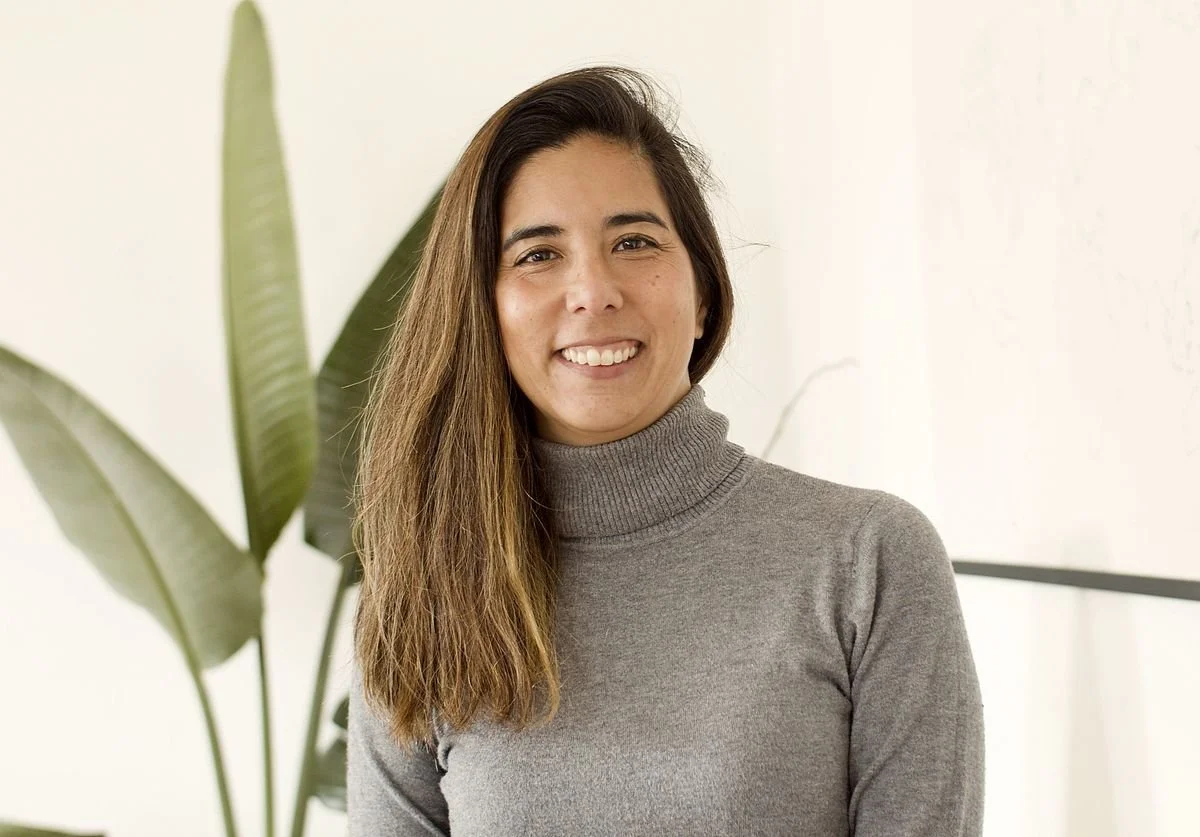 a-woman-posing-against-a-green-plant-and-beige-background-smiling-wellness.jpg