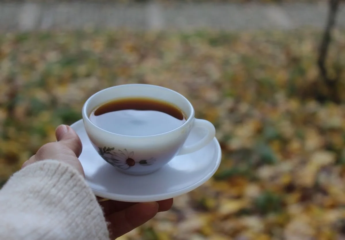 woman-holding-a-cup-of-coffee-on-balmy-autumn-day-outside-with-fallen-leaves-in-the-background.jpg