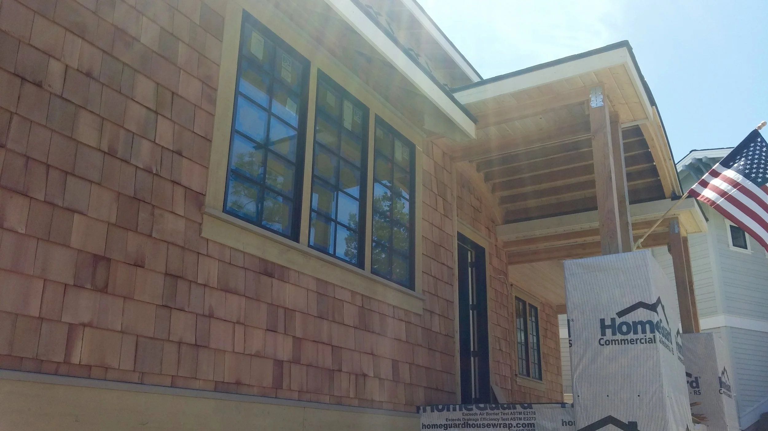 Construction site of a house with brick siding, large windows, and an American flag, during daytime with blue sky.