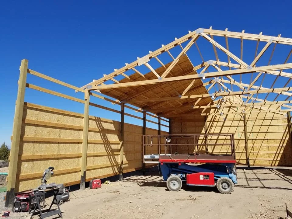 Construction site with a partially built wooden structure, scaffolding, and construction equipment under a clear blue sky.