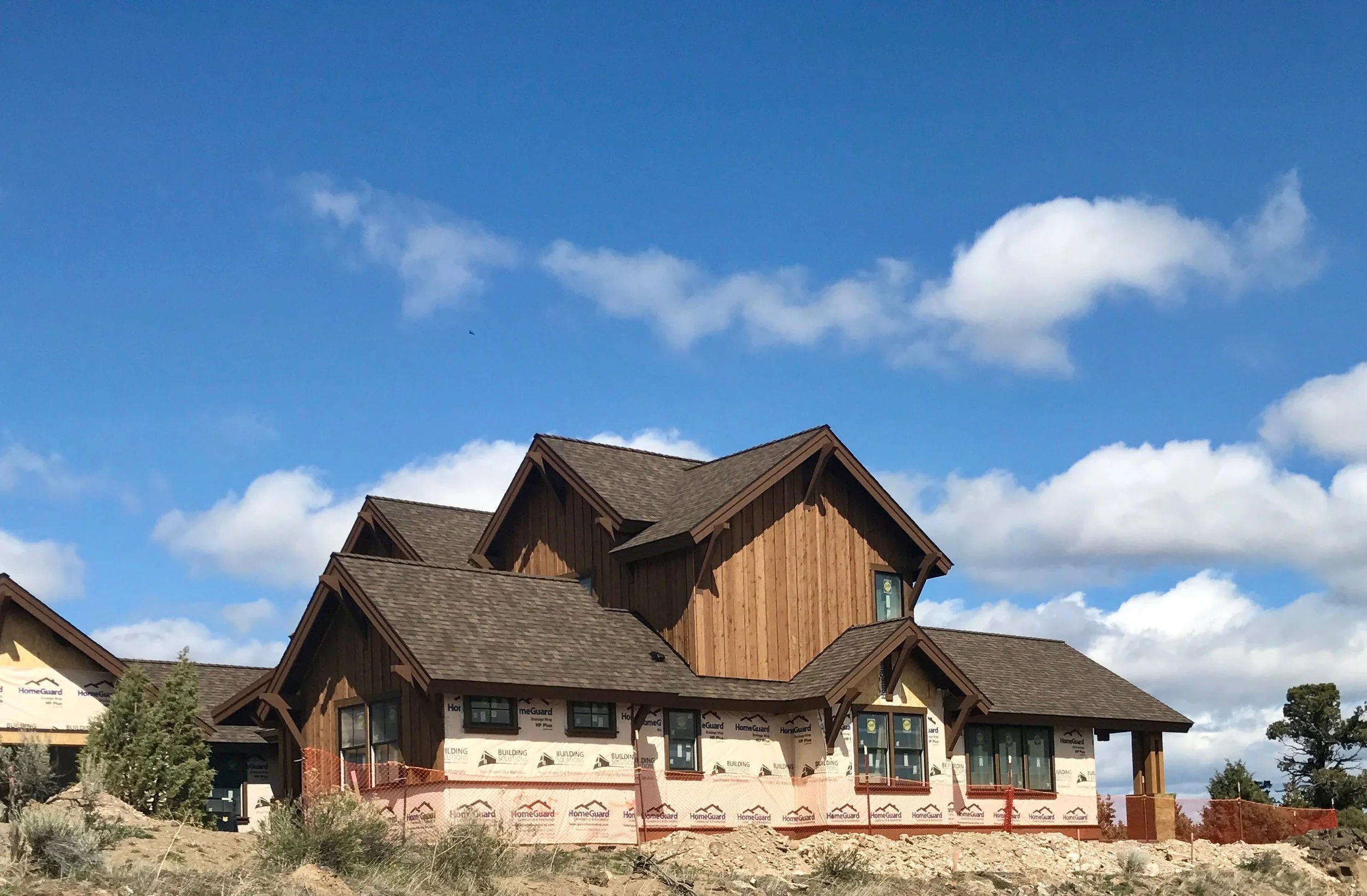Newly constructed house with wooden siding, multiple gable roofs, and large windows, set against a blue sky with clouds.