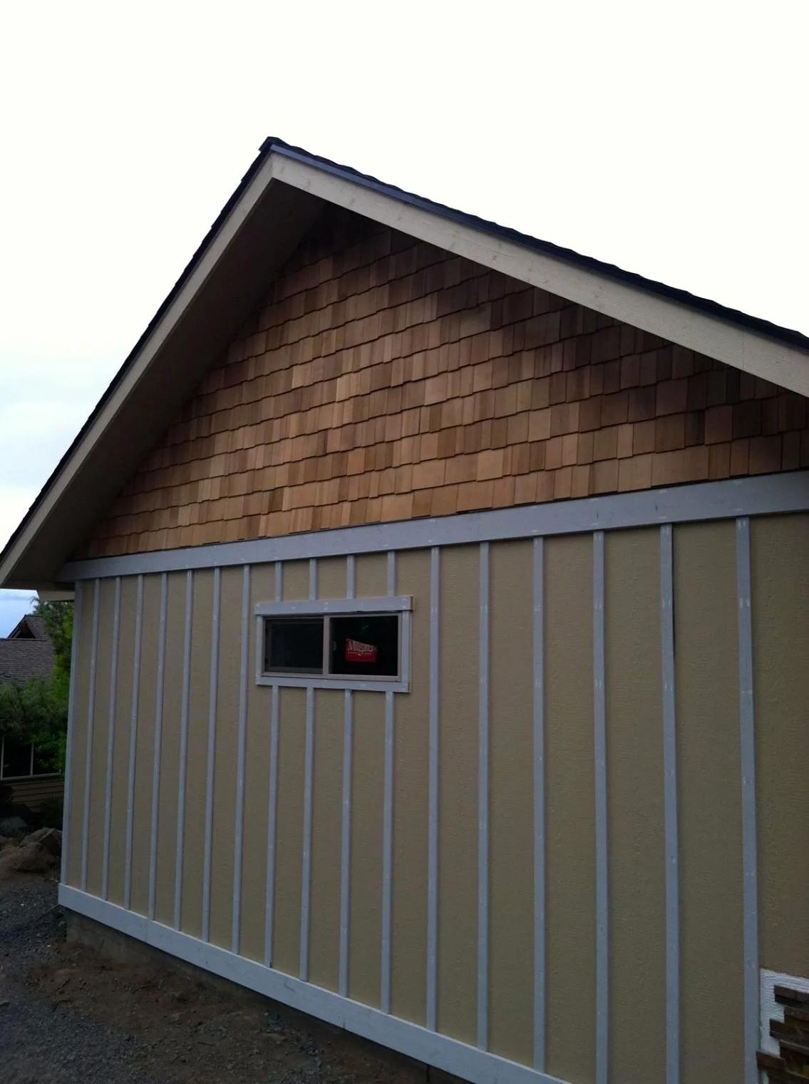 Side view of a house under construction with siding, a small window, and a roof with shingles.