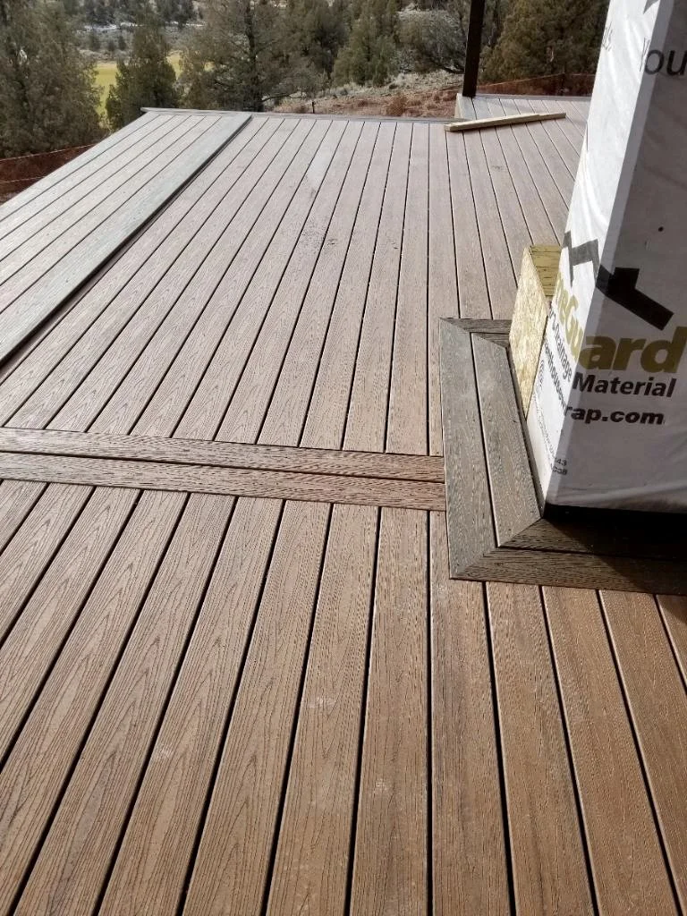 Newly installed wooden deck with interlocking planks and a corner detail around a building foundation.