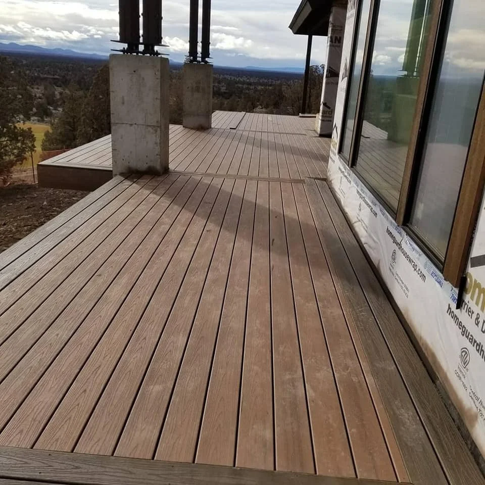 A wooden deck on a building under construction, with support columns and a view of a landscape with trees and mountains in the distance.