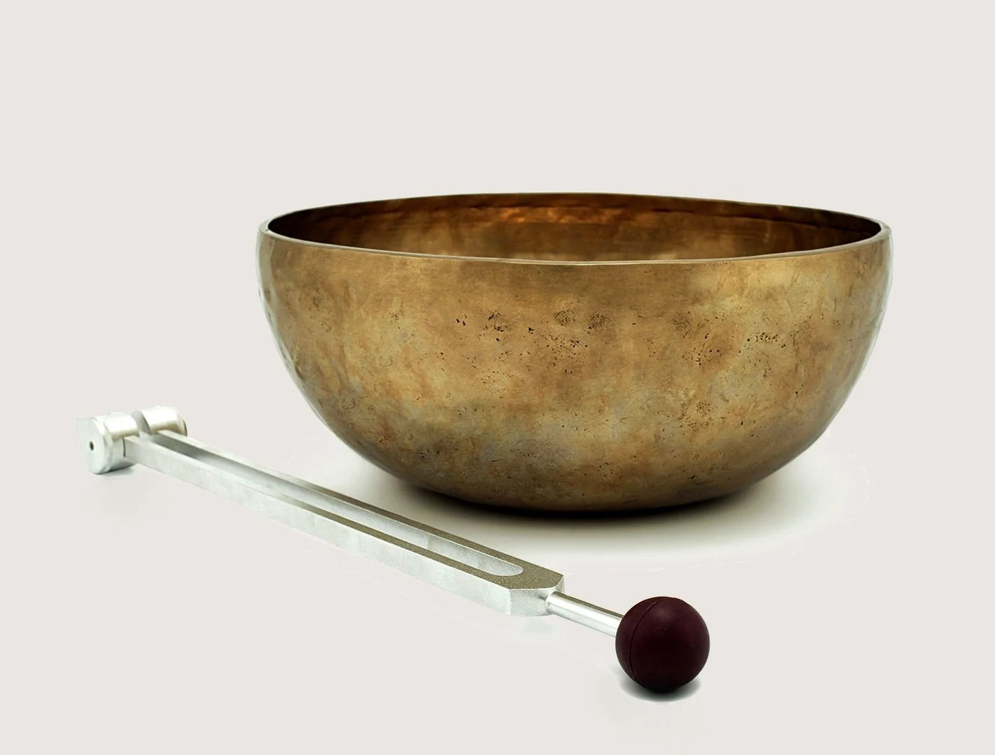 An antique singing bowl with a wooden striker placed beside it on a white background.