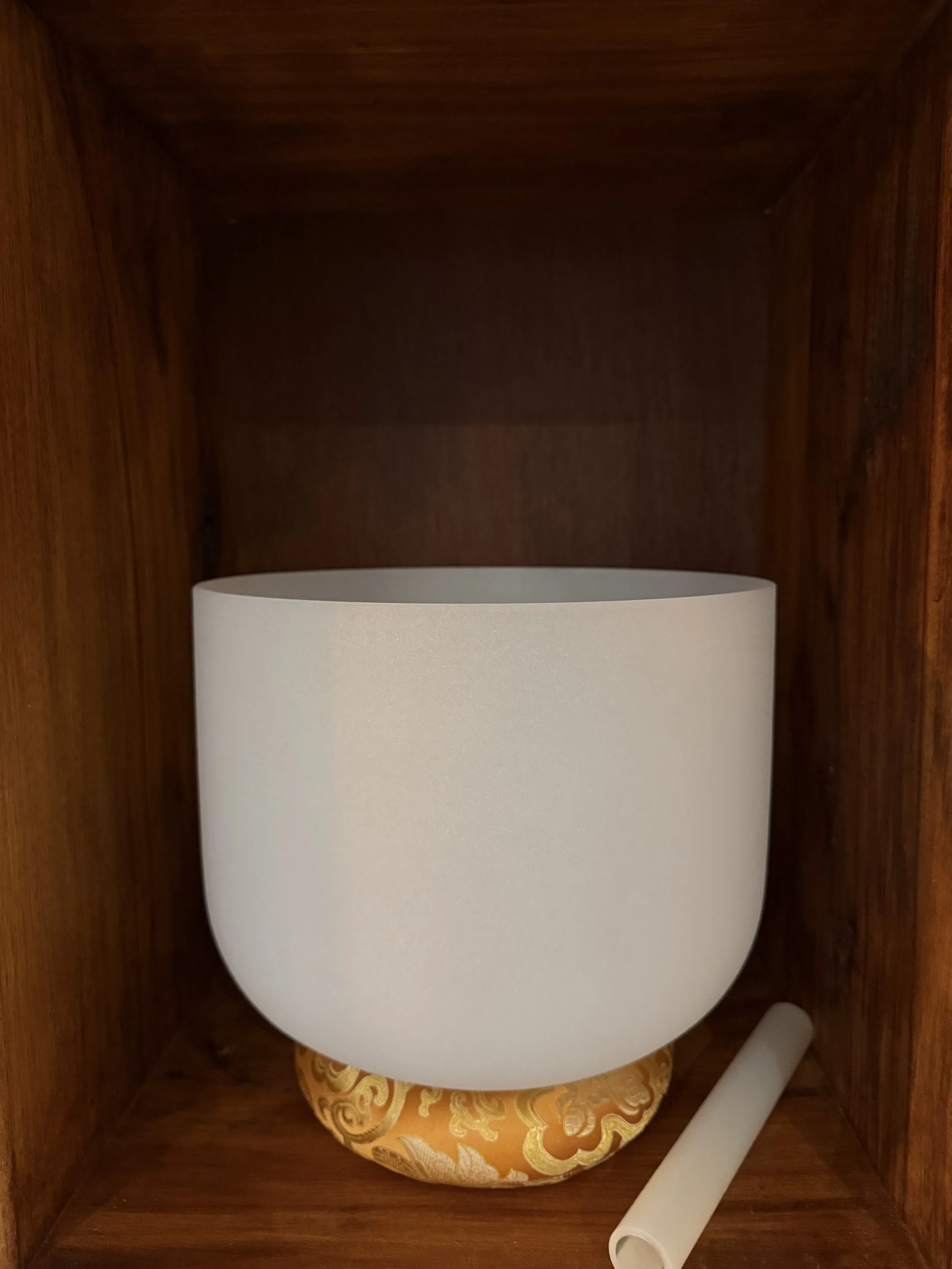 Close-up of a wooden cabinet with a white ceramic bowl, a yellow cloth inside, and a white roll of paper or cloth resting on the bottom.