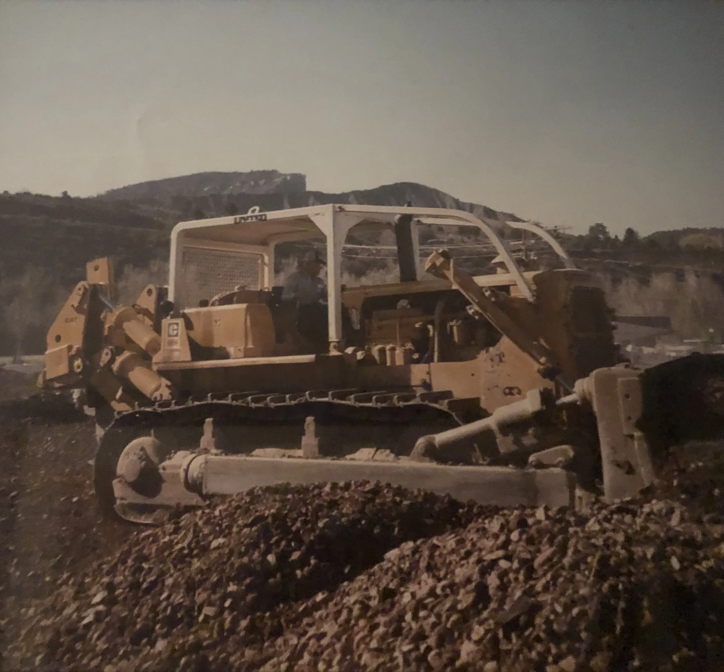Nighttime scene with construction equipment, possibly a bulldozer, on a gravel or dirt surface, hills in the background under a dark sky.