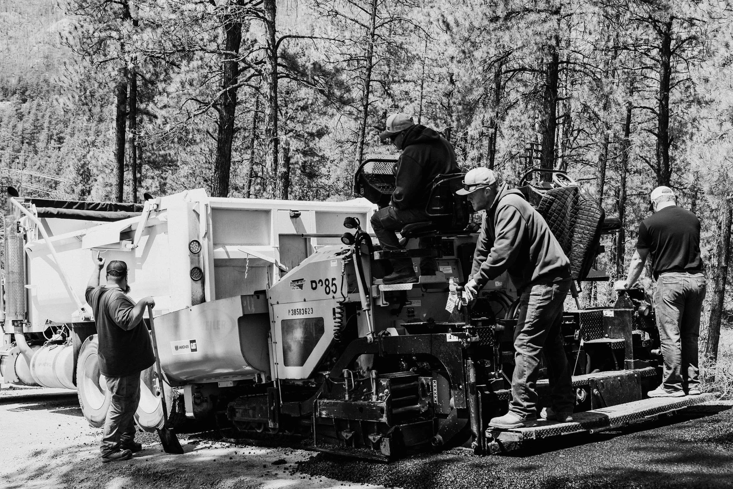 Workers operating heavy machinery on a construction site surrounded by trees.
