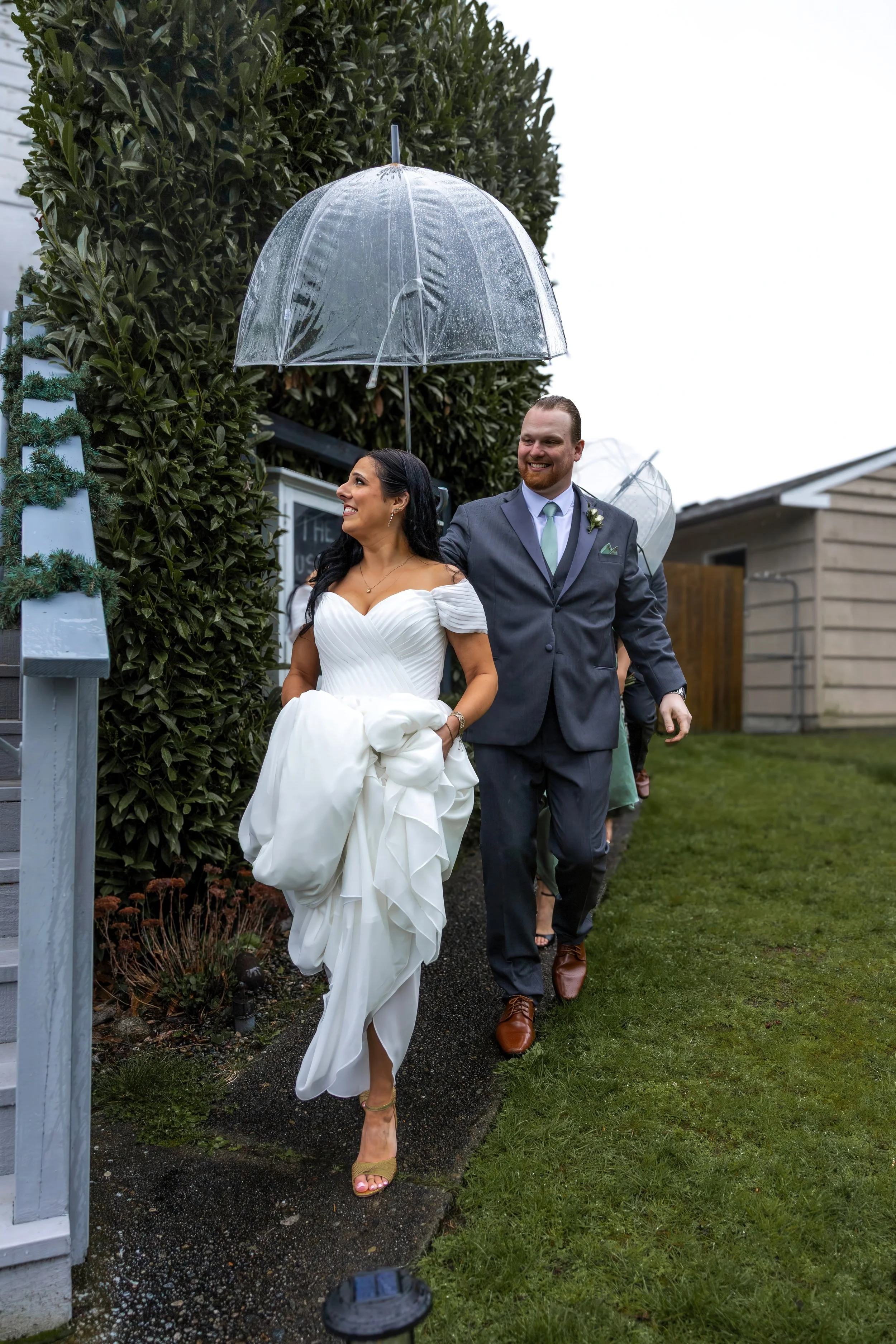 bride and groom leaving a wedding under a transparent umbrella on a rainy day