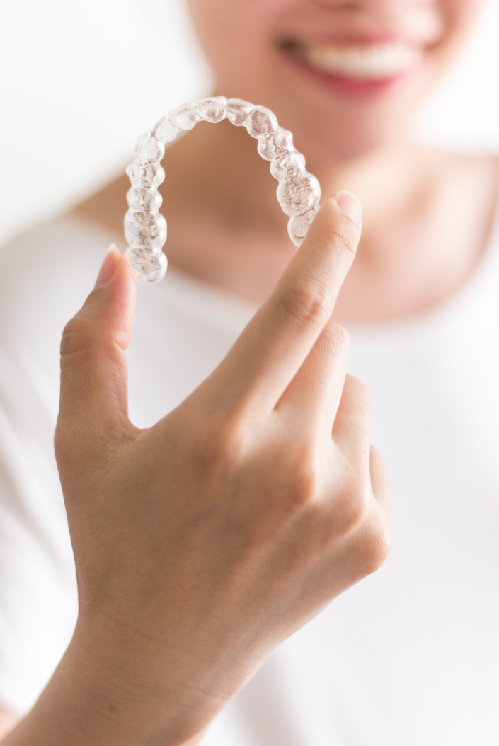 Person smiling and holding a clear dental aligner.