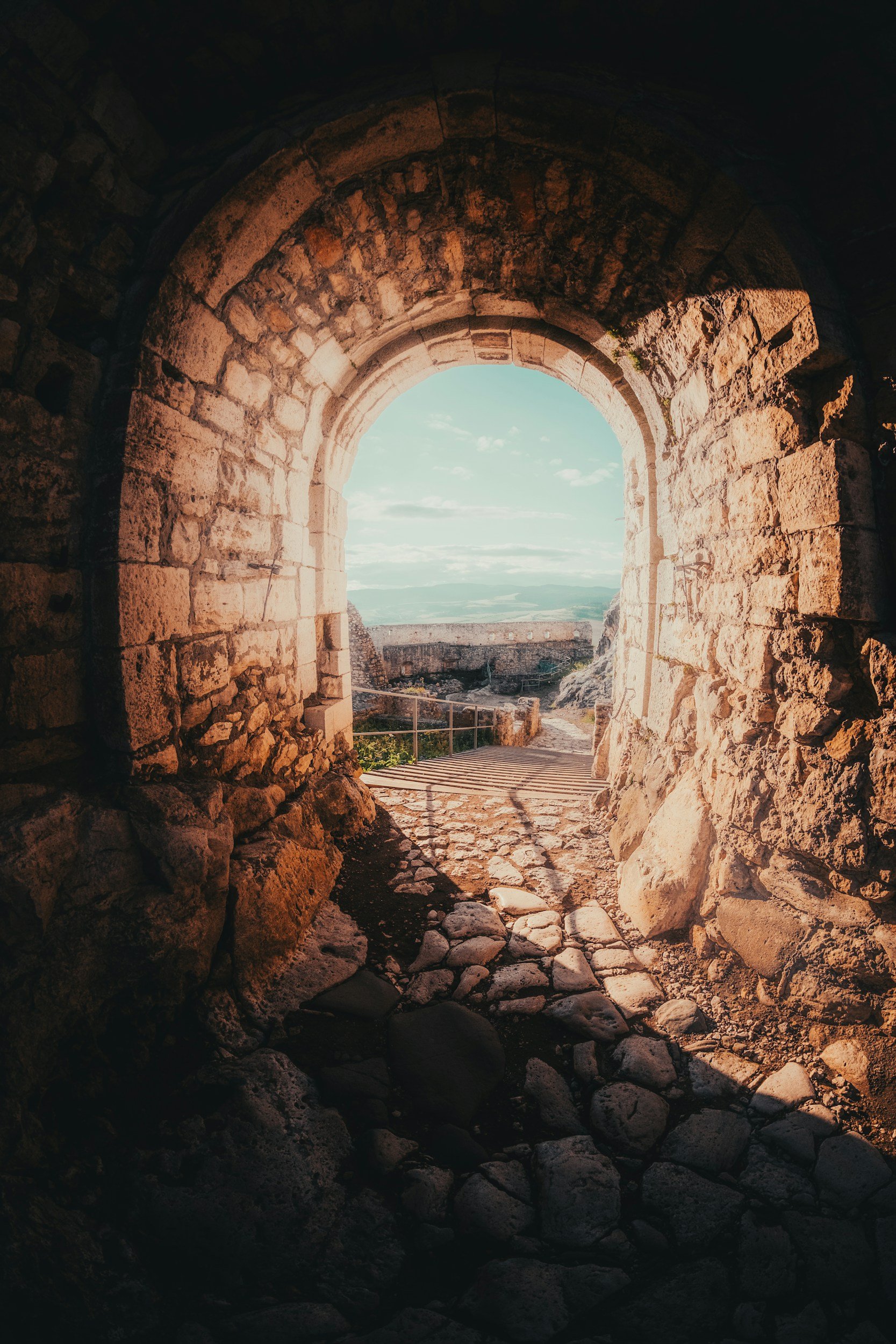 View through an ancient stone archway opening to a landscape with hills and a cloudy sky.