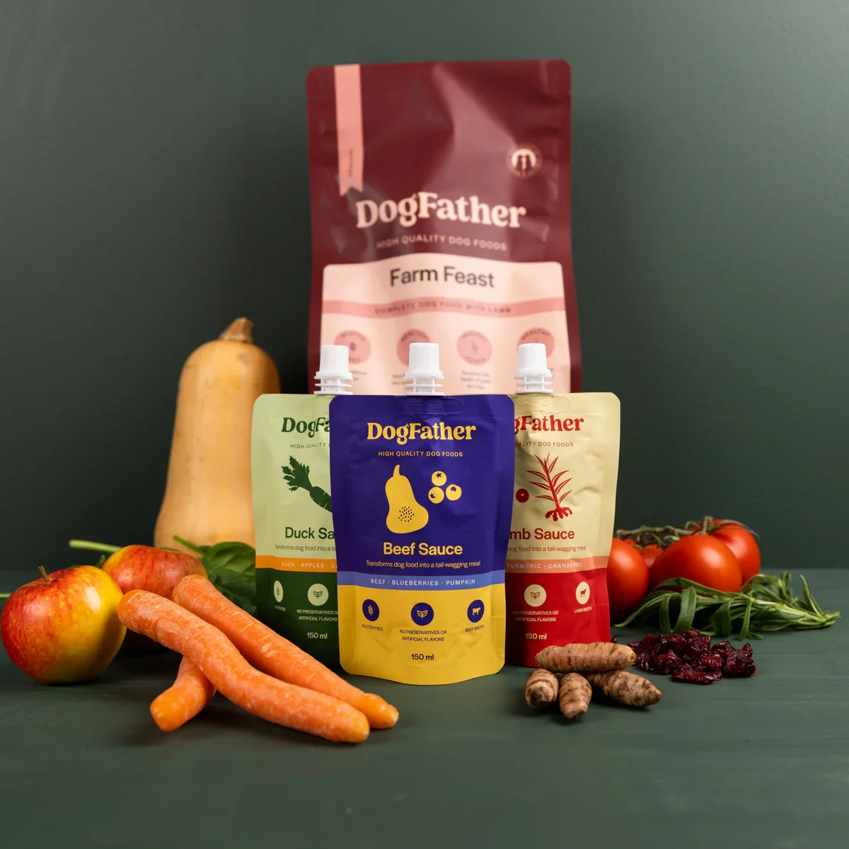 Hundmatprodukter av märket DogFather med olika smaker, omgivna av färska grönsaker som äpplen, morötter, tomater, en pumpa, ingefära, hjortron och rucola.