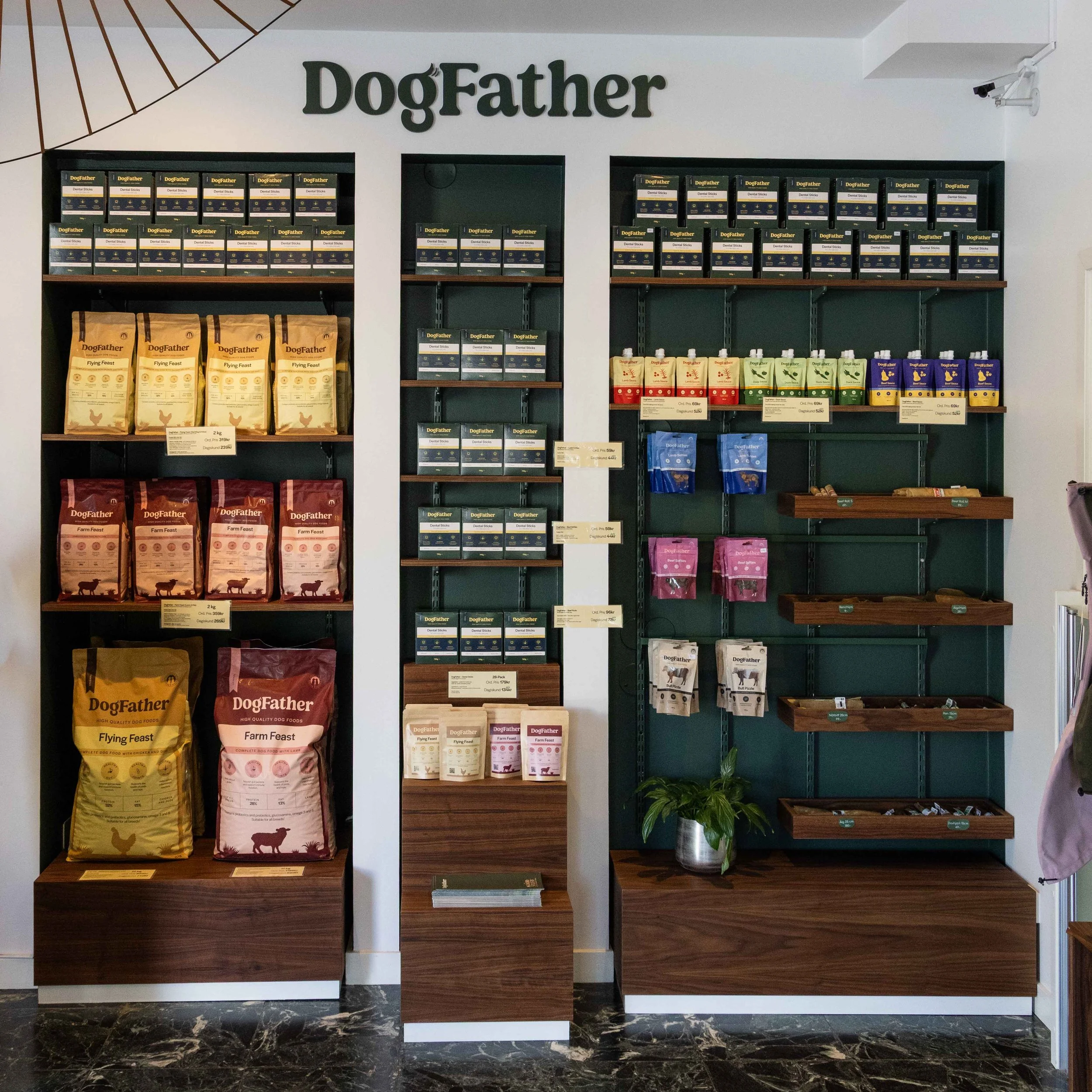 Inredning i ett butikskoncept för hundmat, med hyllor fyllda med DogFather-bröd, på en vägg med skylten 'DogFather' i stora bokstäver.