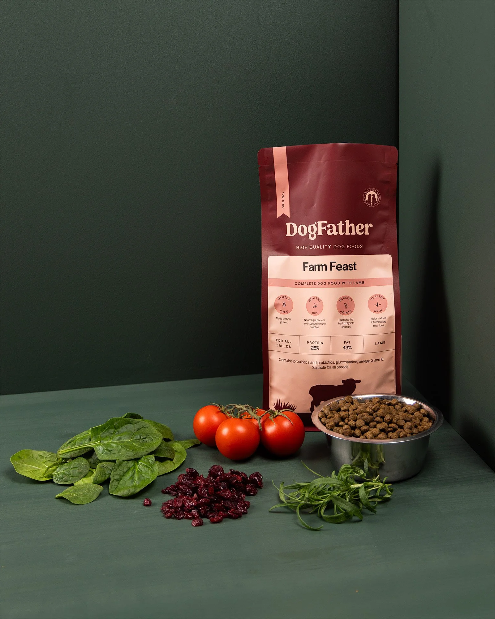 Bild på en påse dog food (DogFather Farm Feast) med färska tomater, spenat, örter, torkad hundmat, och andra gröna bladgrönsaker framför.
