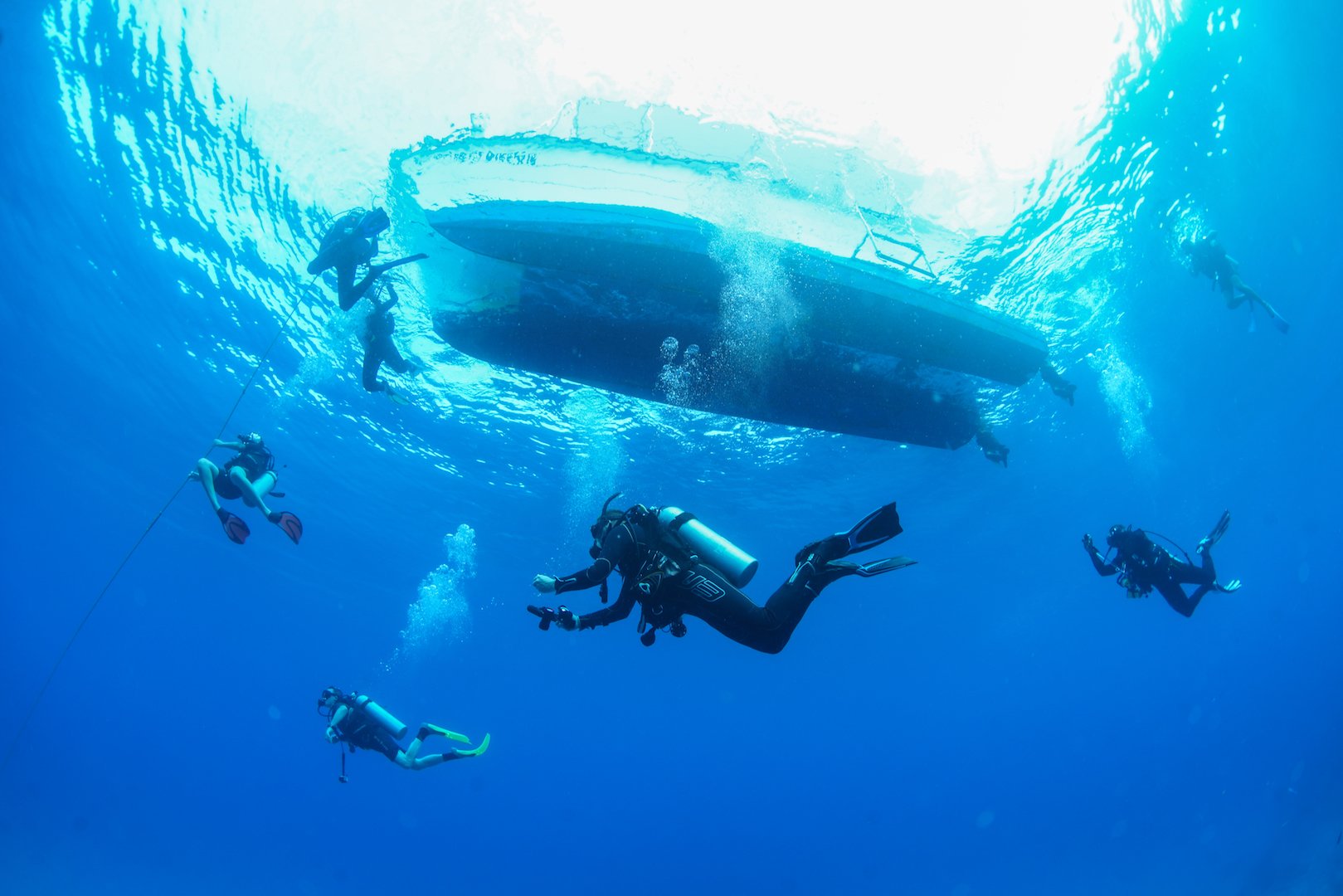 Seven scuba divers underwater near the side of a boat.