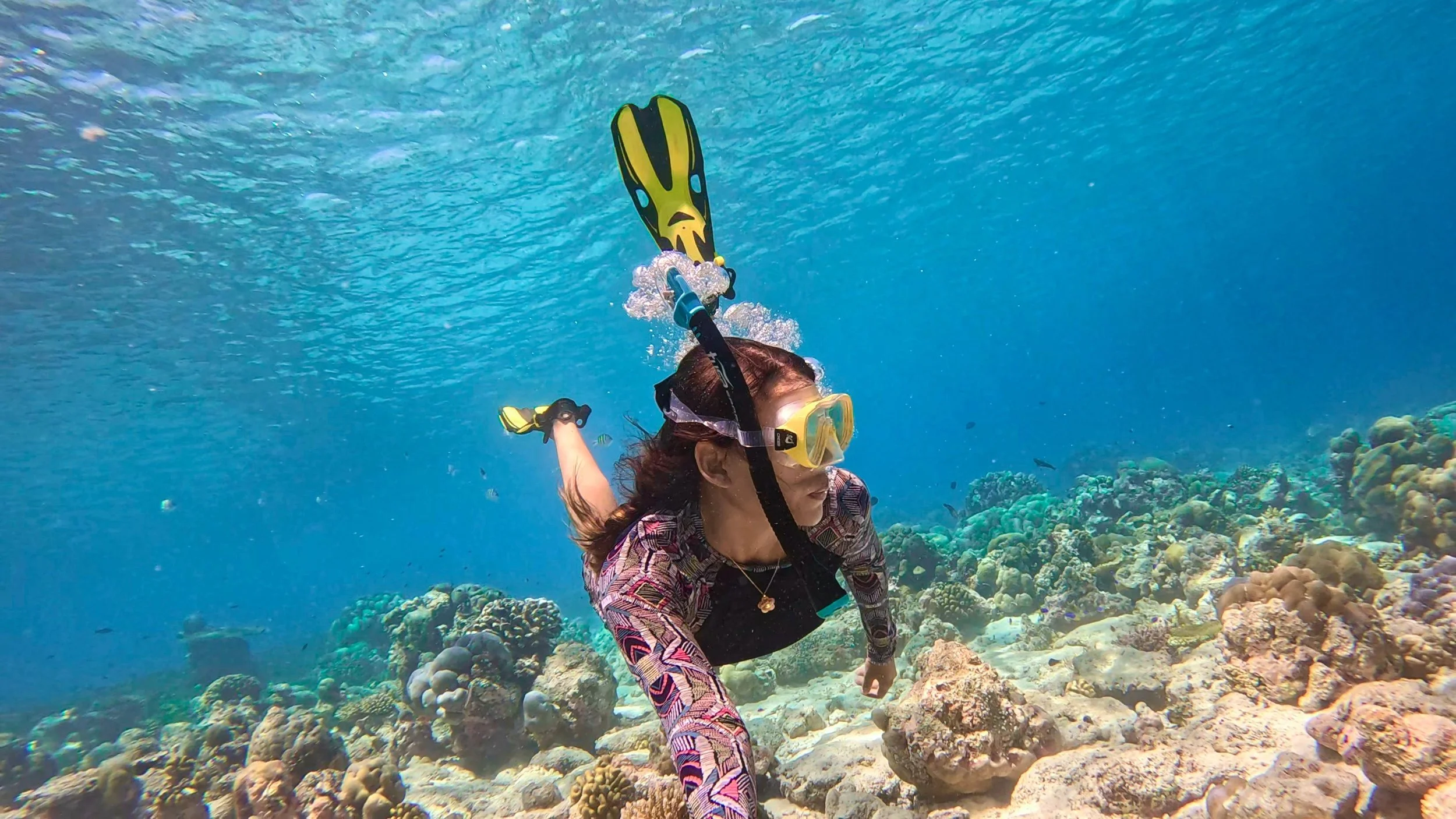 A woman with dark curly hair sitting on a bench, writing in a notebook, with a modern abstract painting and a wooden wall in the background, illuminated by sunlight.