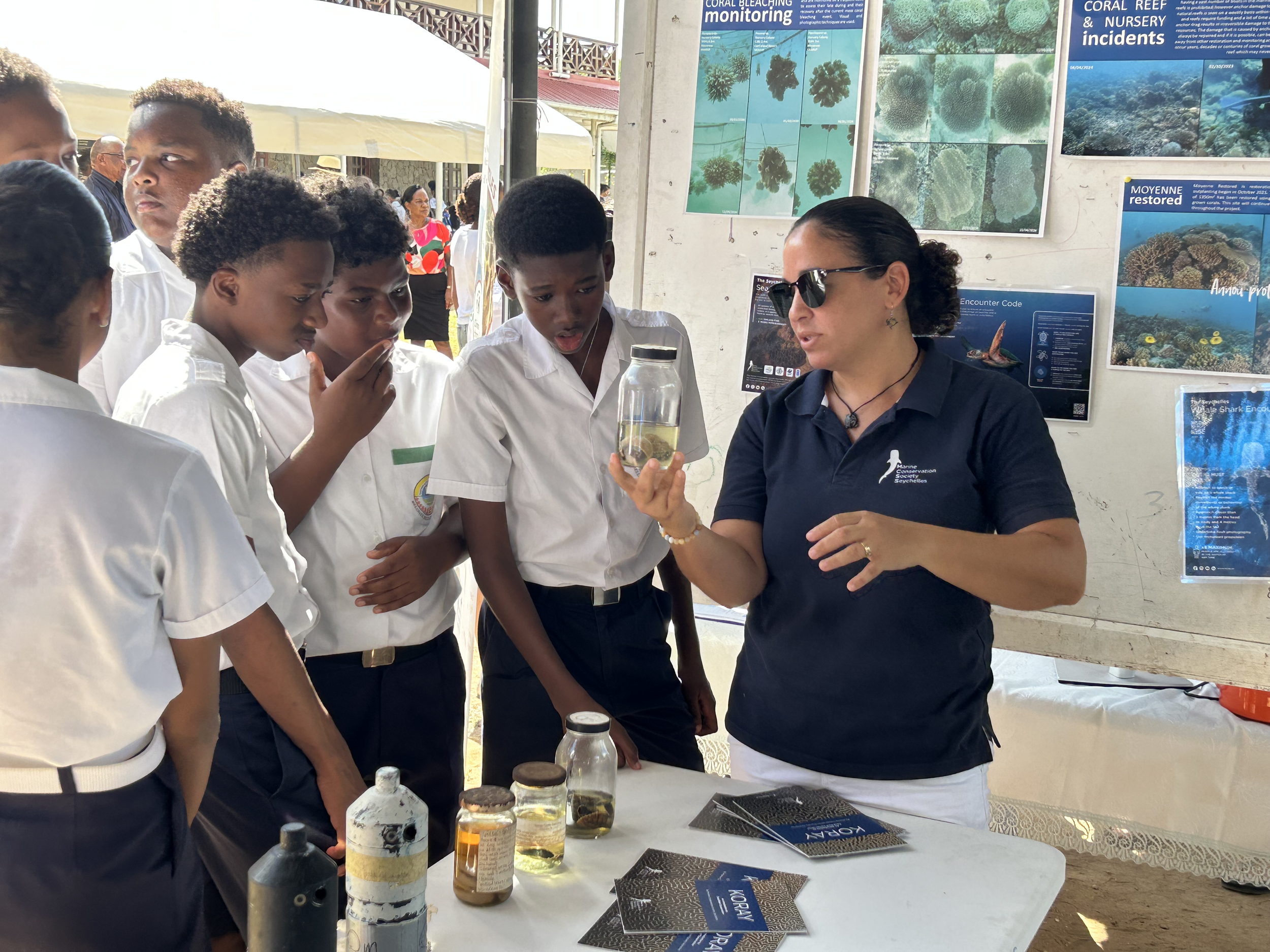 A woman explaining marine conservation to a group of school children at an educational exhibit about coral reefs, sea life, and ecological restoration.