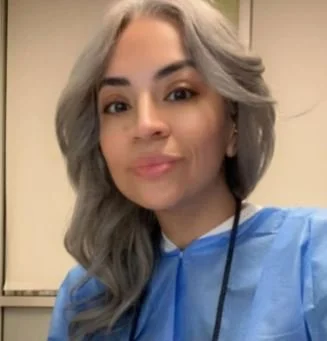 A woman with silver hair wearing a blue medical gown indoors.
