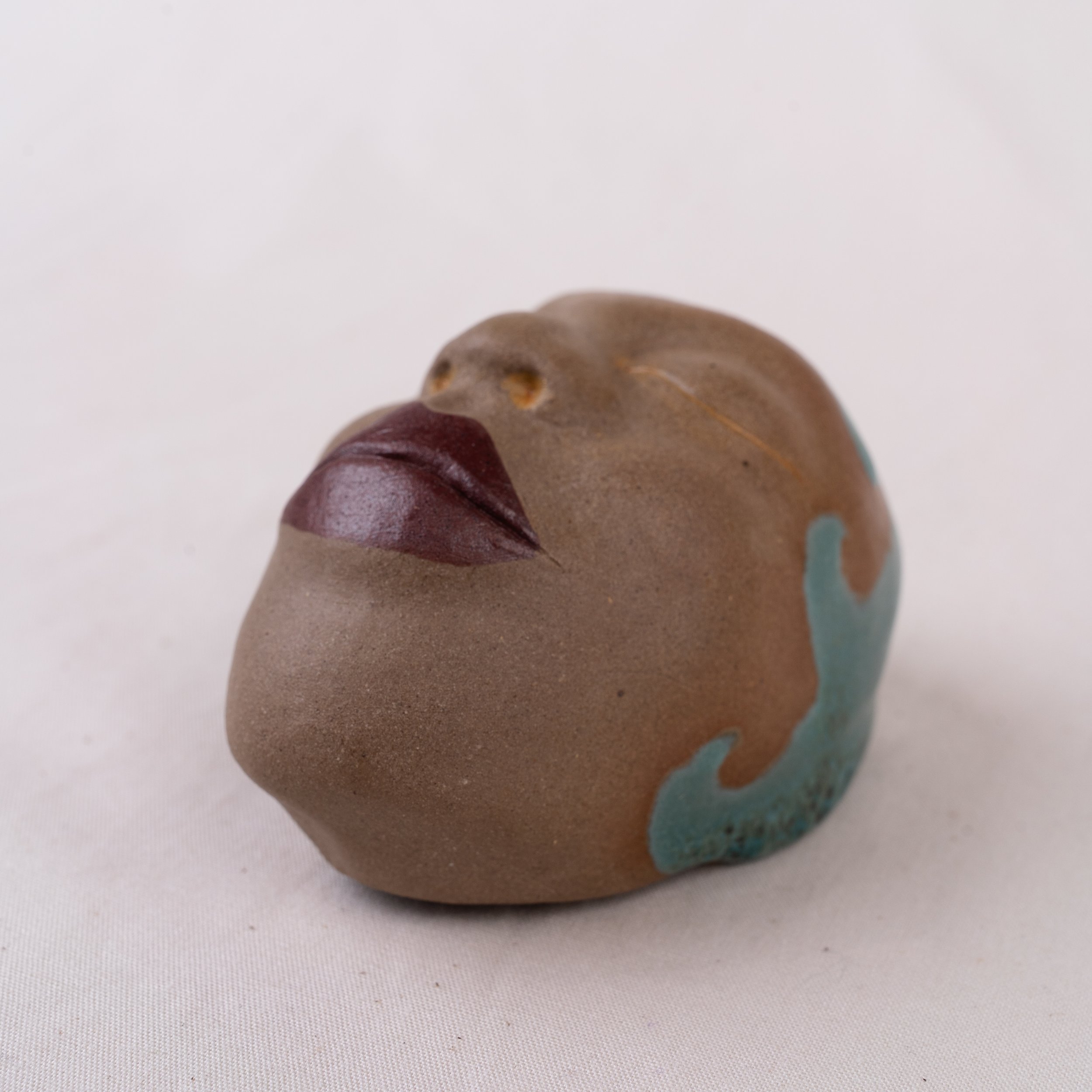 Close-up of a small face sculpture, set against a white background.