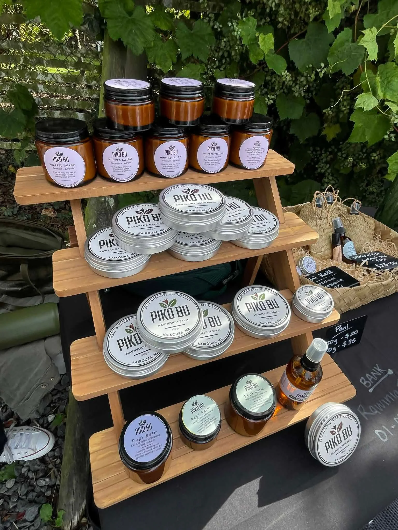 Display of natural skincare products on a wooden stand, including balms and sprays, with various labels and a chalkboard sign nearby.
