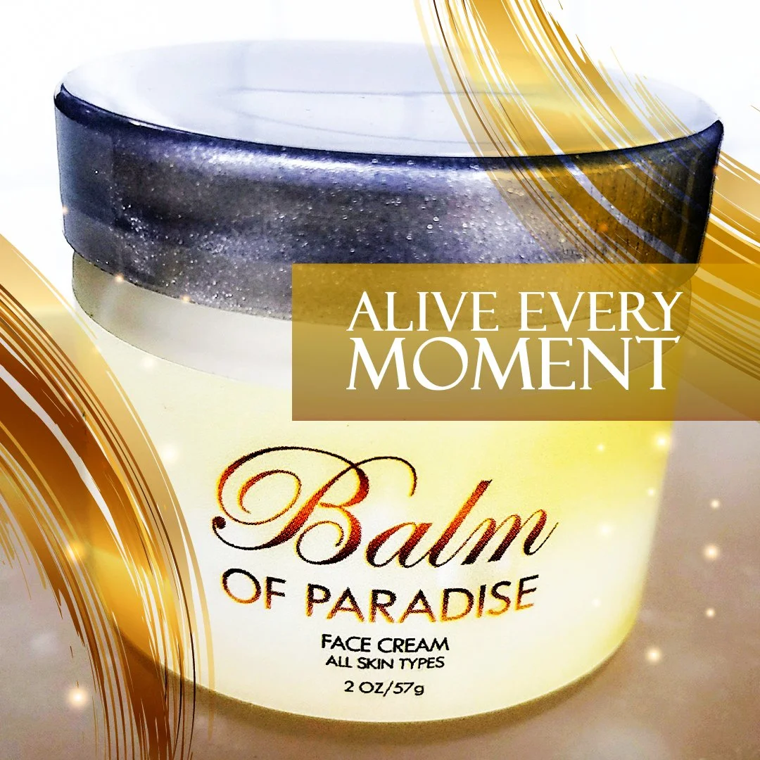 A container of Balm of Paradise face cream with a dark silver lid, featuring white, gold, and brown text, and gold design accents, with the slogan 'Alive Every Moment' on the label.