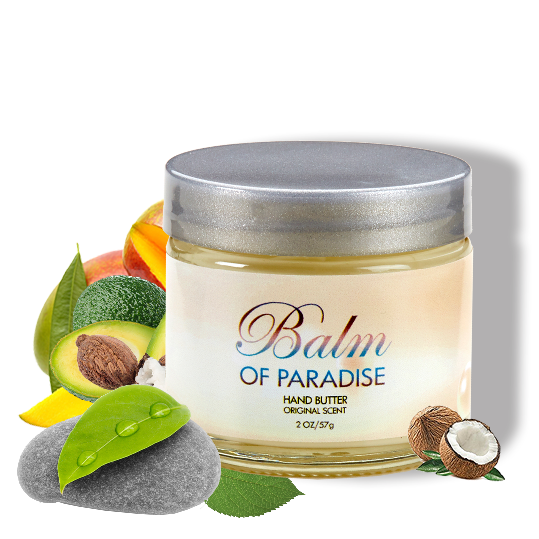 A jar of Balm of Paradise hand butter with a silver lid, surrounded by tropical fruits including avocado, coconut, mango, lime, and peach, along with green leaves and smooth stones.