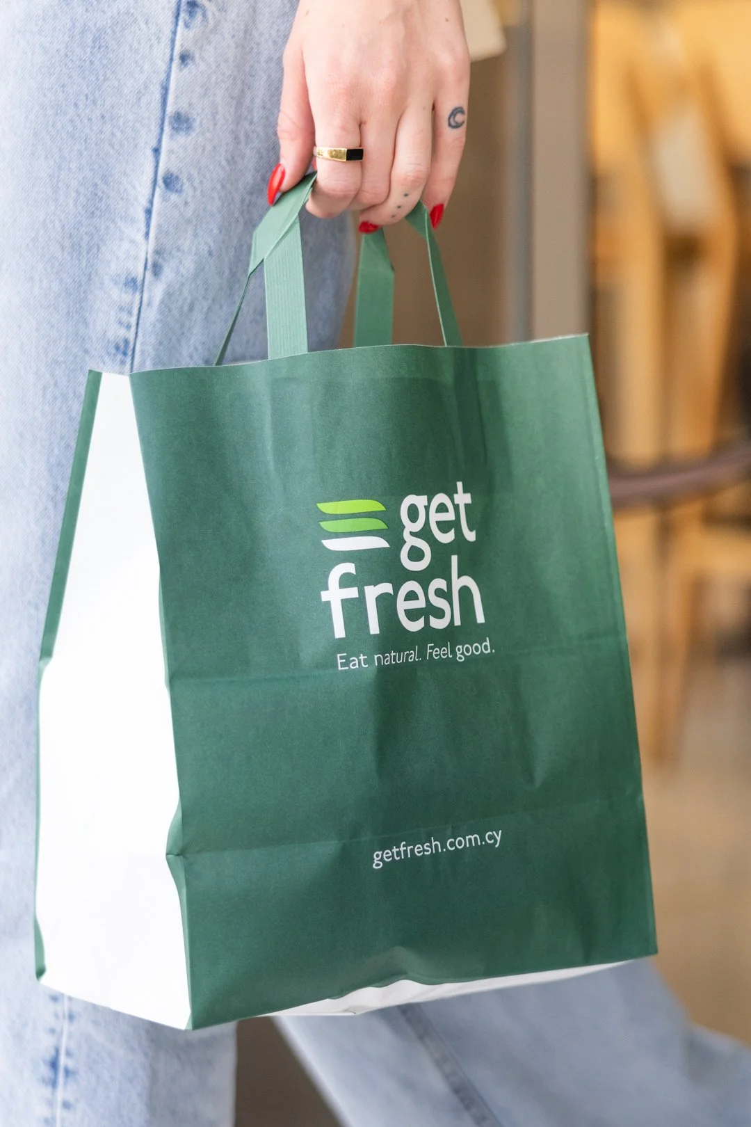 A stylish , cool girl holding a green paper shopping bag with the logo and text 'get fresh' and the slogan 'Eat natural. Feel good.' on it.