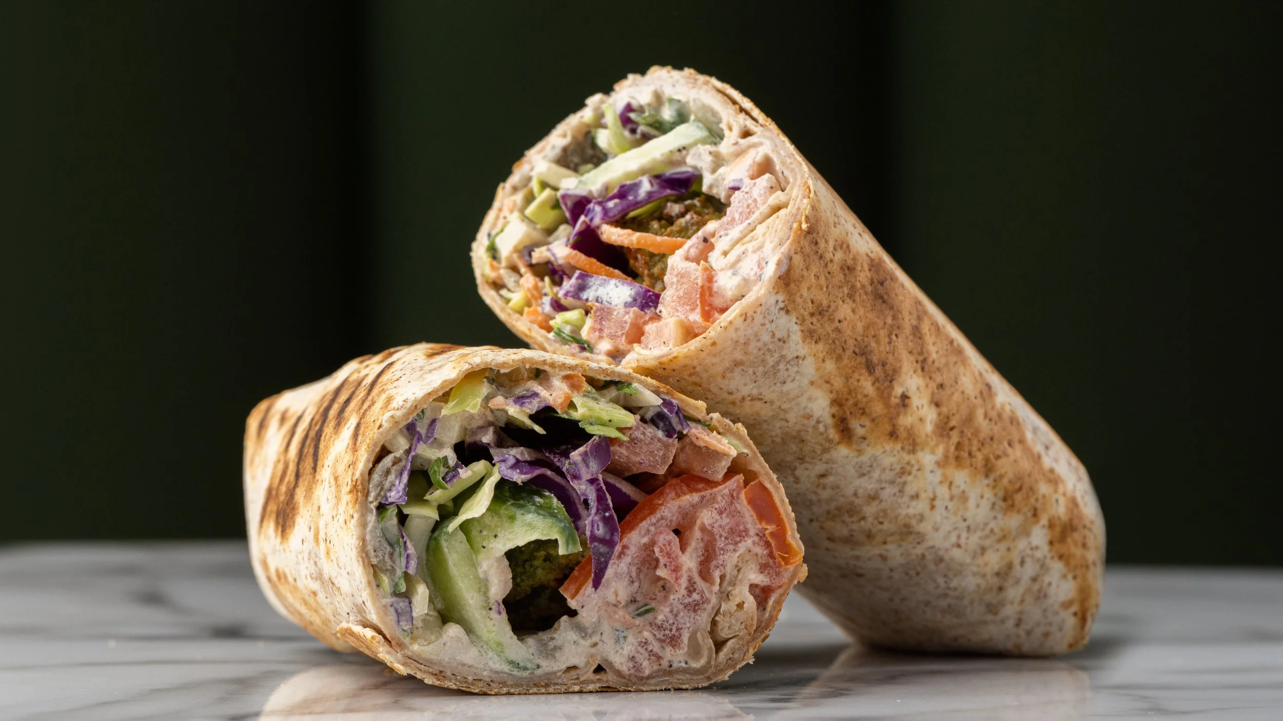 Delicious falafel wrap, showing colorful vegetables and filling inside a toasted flour tortilla. Healthy, light lunch
