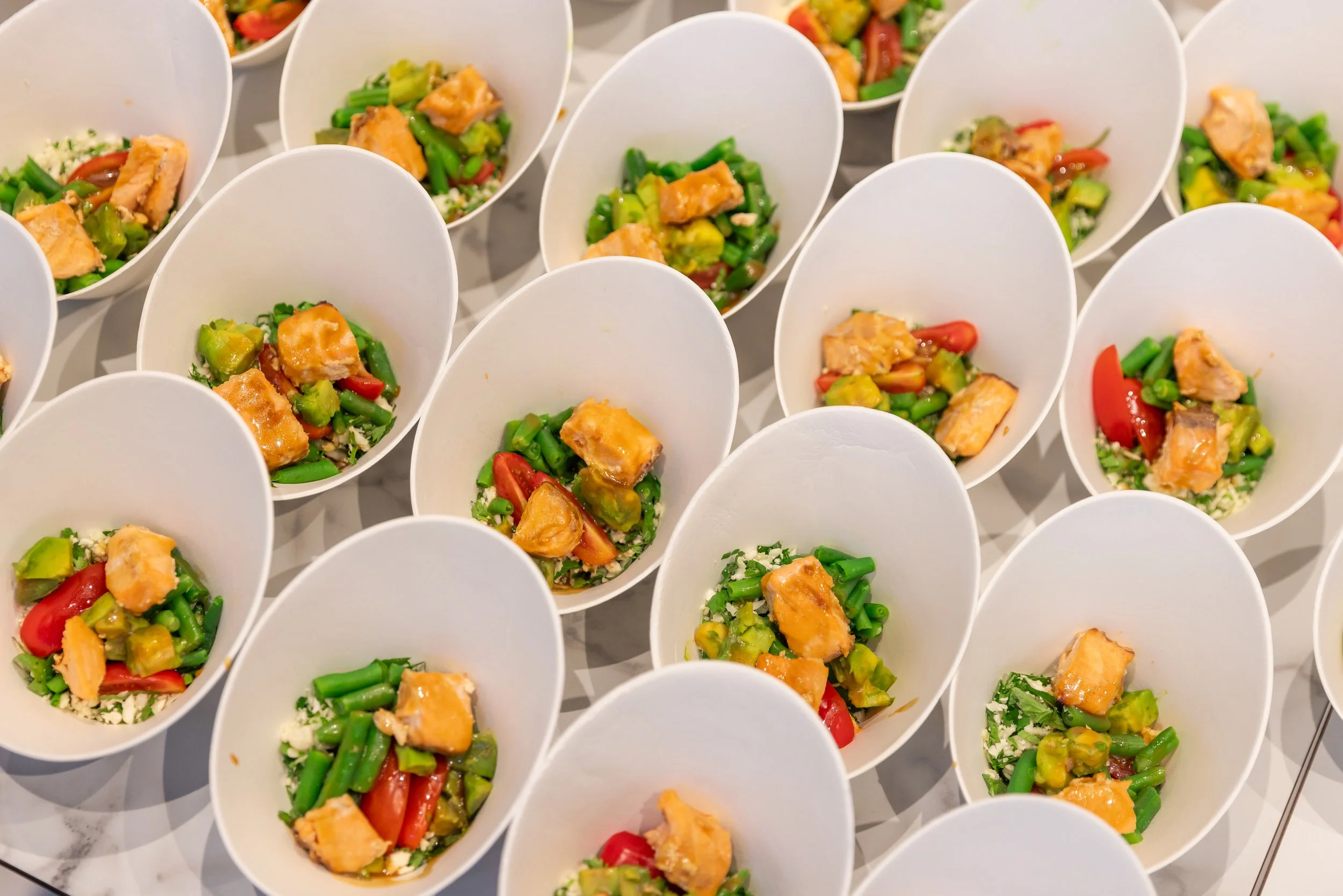 Multiple white cups filled with colorful chopped vegetables and pieces of cooked chicken arranged on a flat tray, viewed from above. Get Fresh catering, healthy, delicious, clean food.